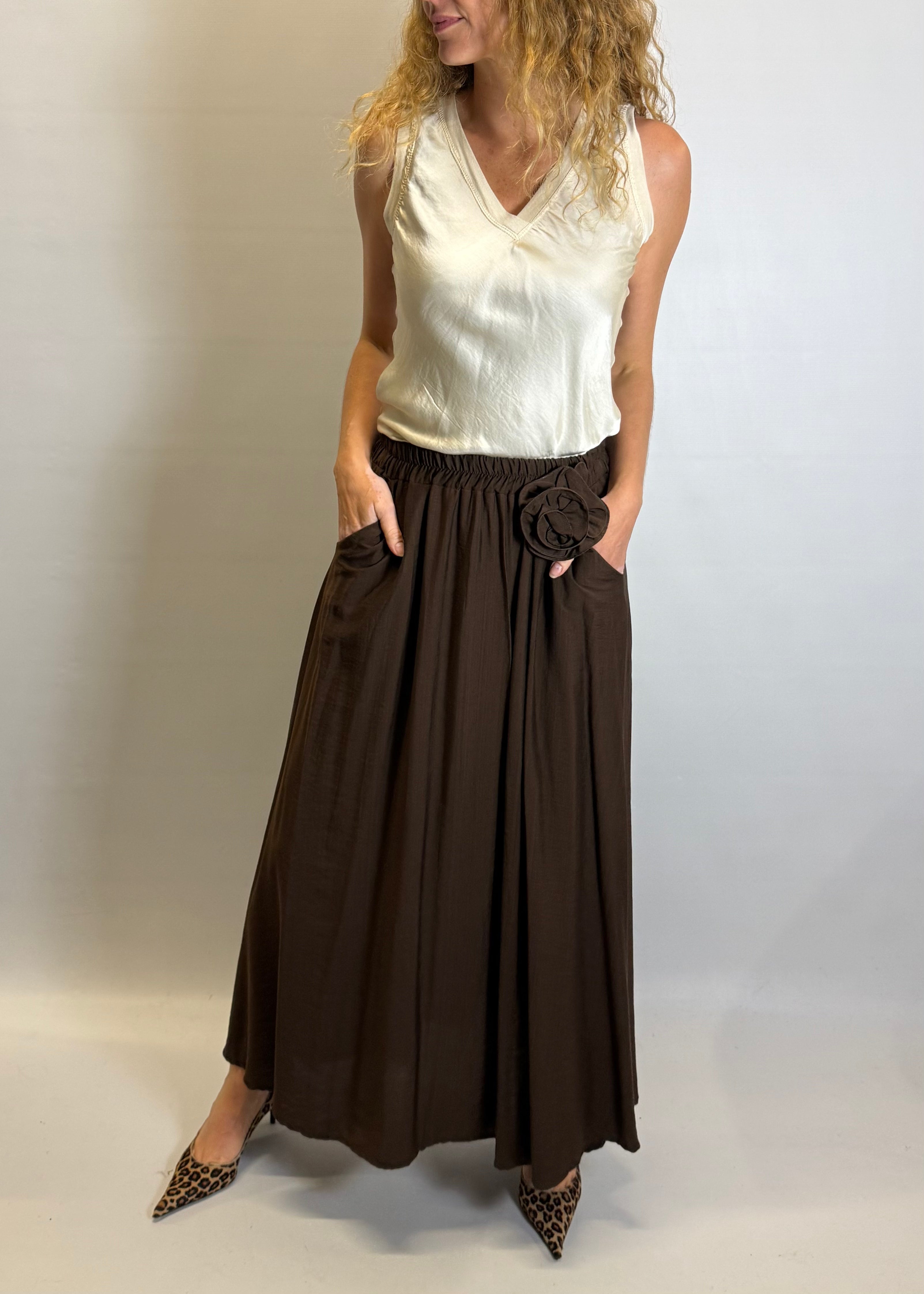 Woman wearing a white sleeveless top and brown wide-leg pants against a plain background