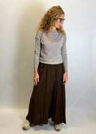 Person wearing a gray sweater and brown wide-leg pants against a plain background
