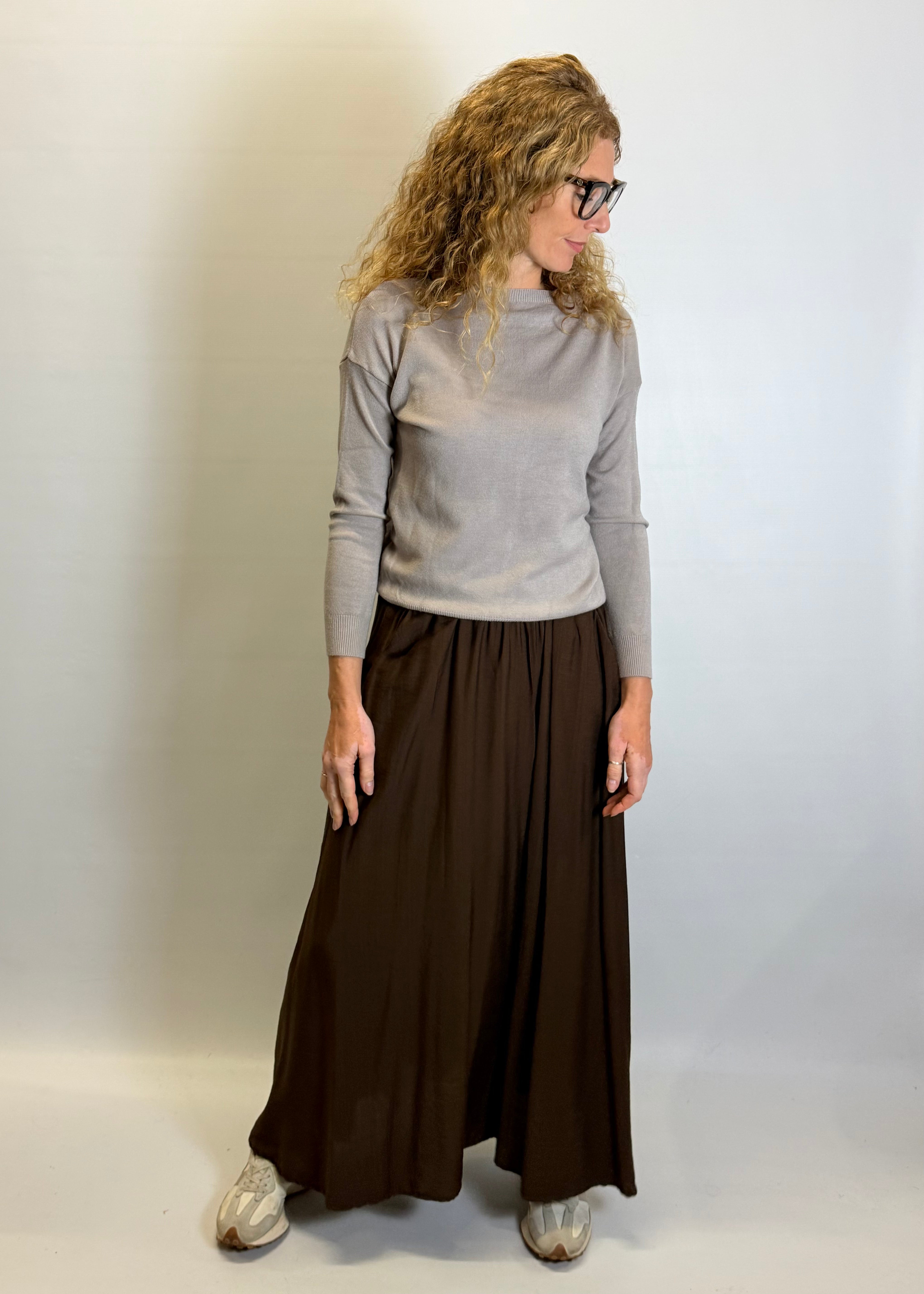 Person wearing a gray sweater and brown wide-leg pants against a plain background