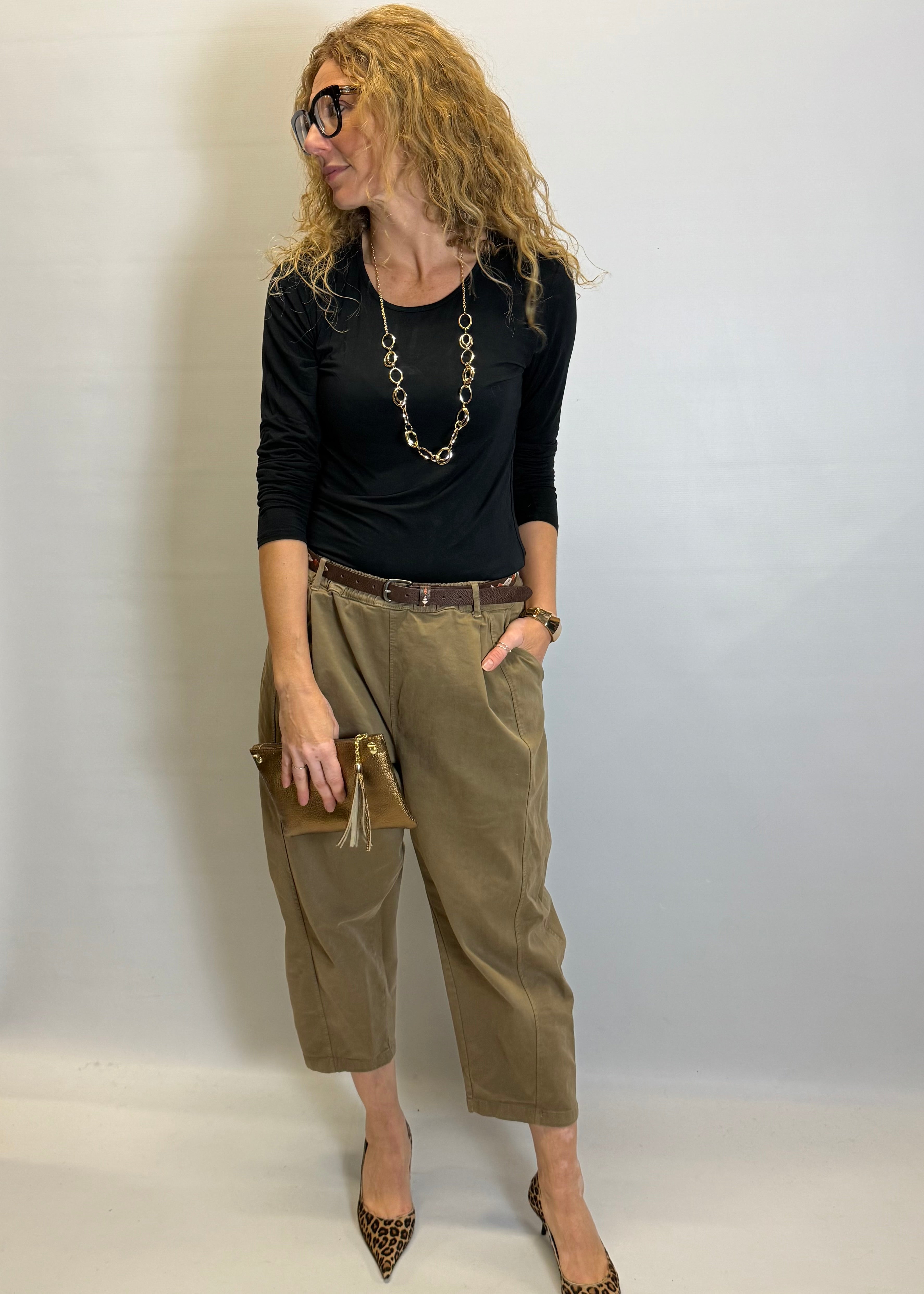 Woman wearing a black top, olive green pants, and leopard print shoes against a plain background