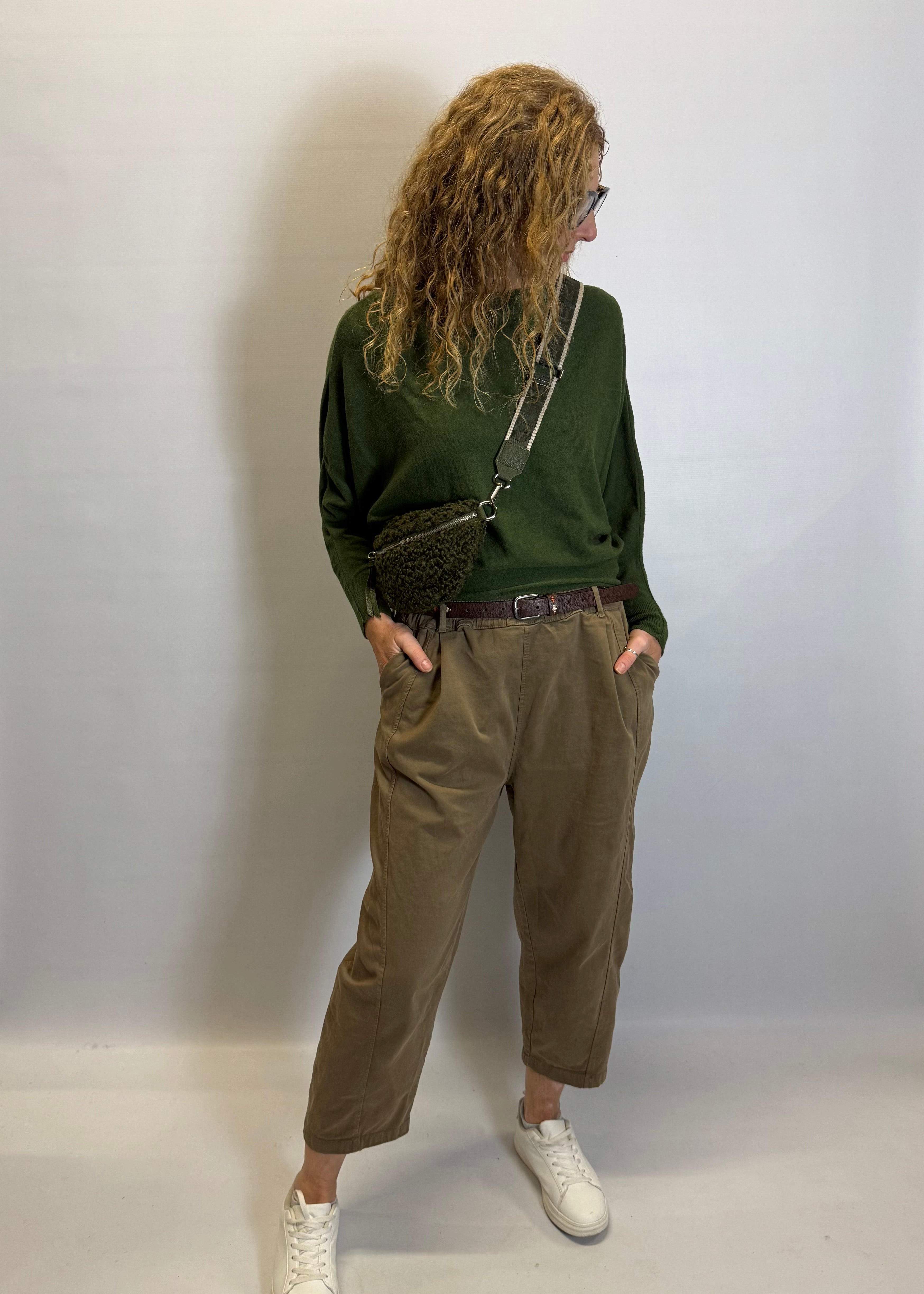 Person wearing a green sweater and brown pants against a plain background