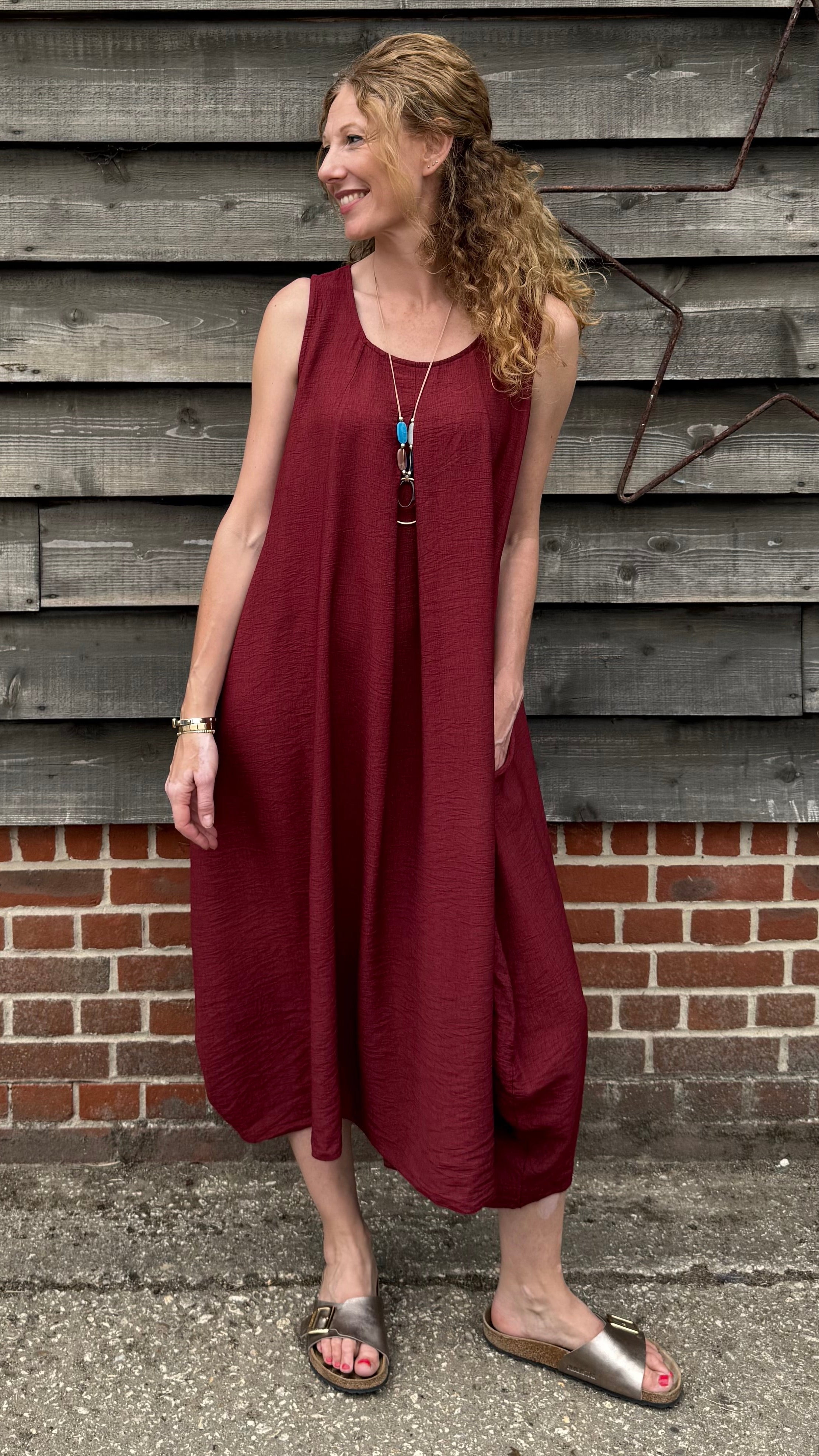 Woman in a burgundy dress standing against a wooden wall.