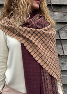 Person wearing a large plaid scarf in front of a wooden background