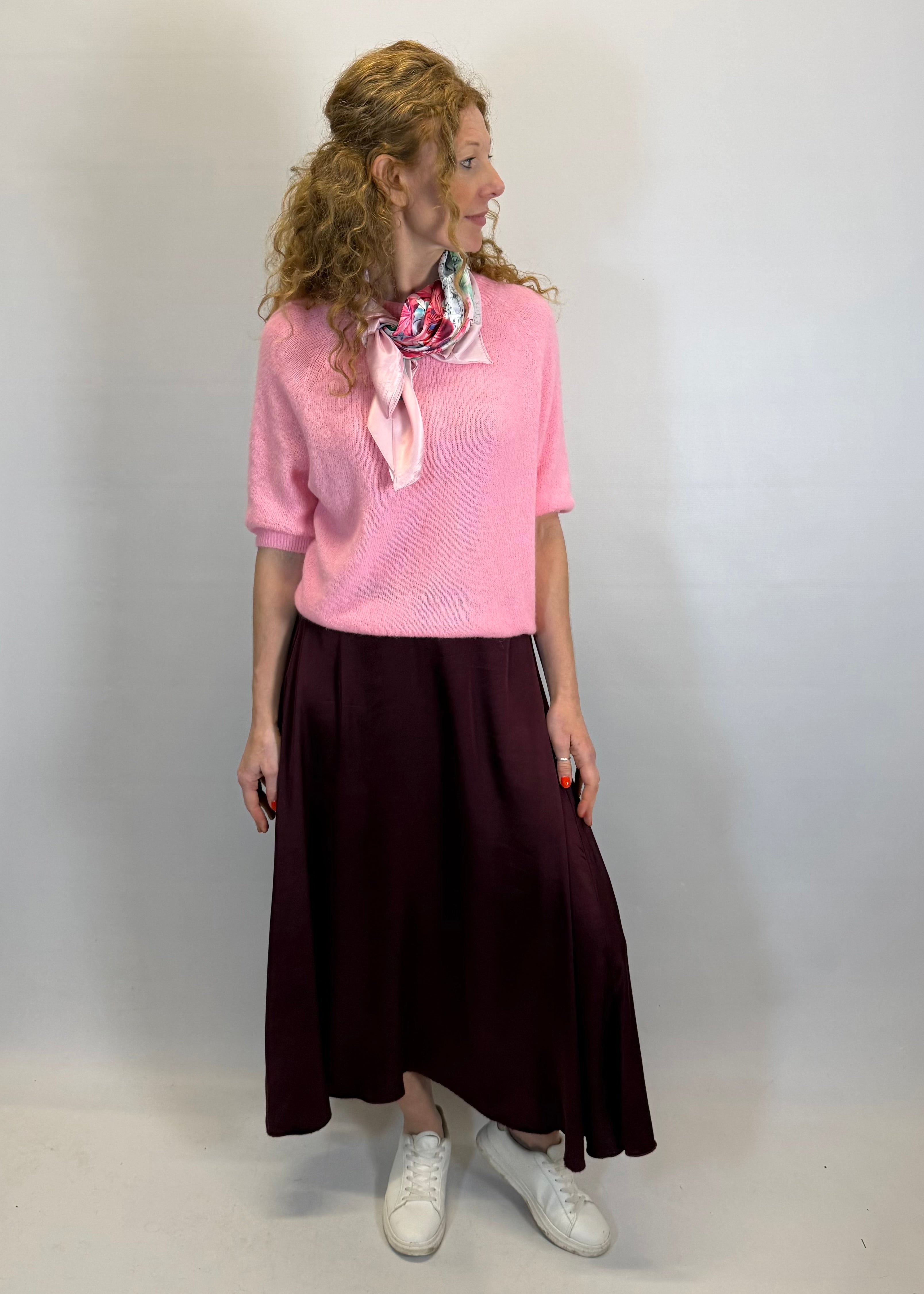 Woman wearing a pink sweater and dark skirt with a white background