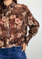 Person wearing a floral patterned blouse with long sleeves on a plain background