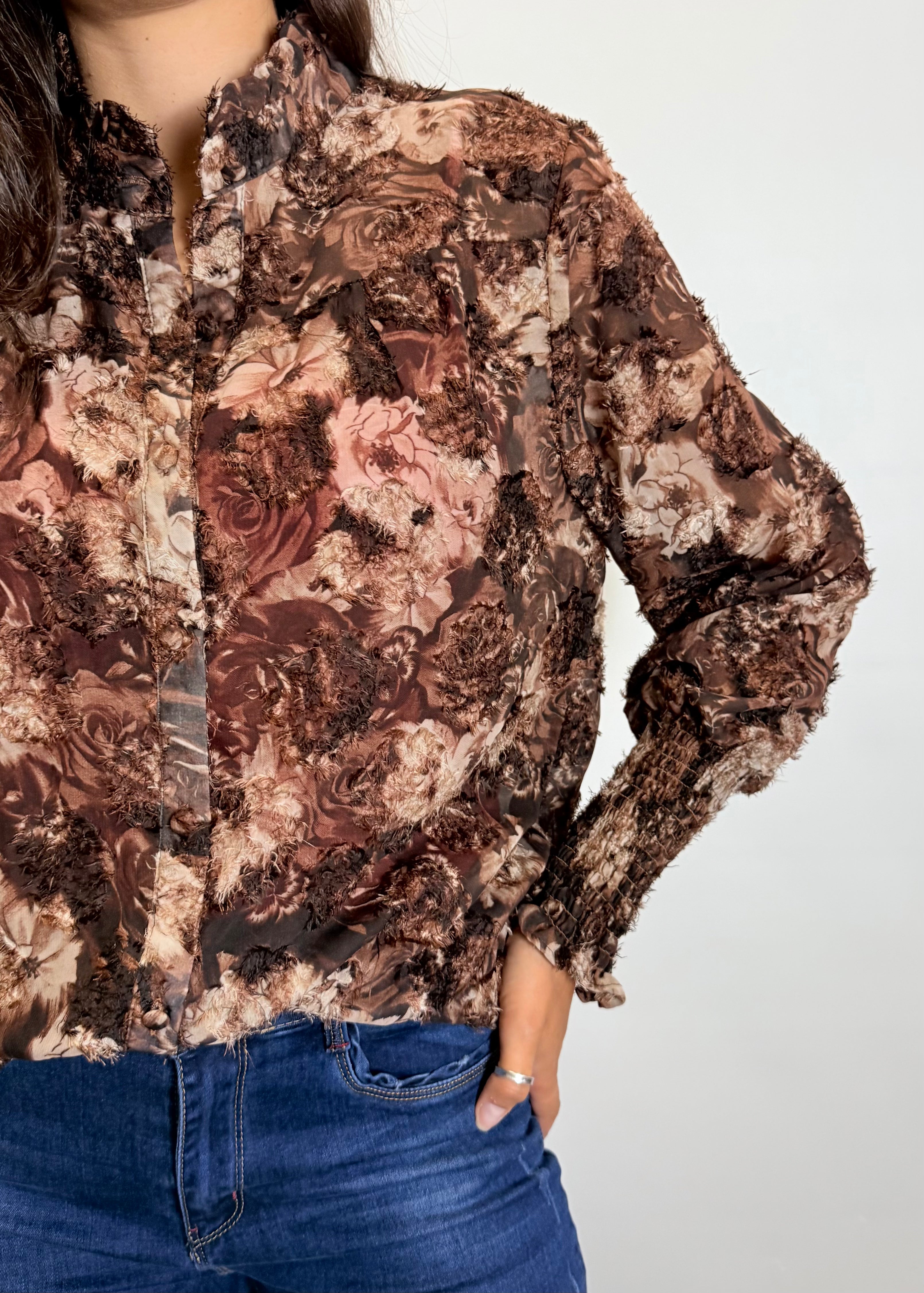Person wearing a floral patterned blouse with long sleeves on a plain background