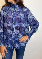 Woman wearing a blue floral blouse, jeans, and brown boots against a plain background