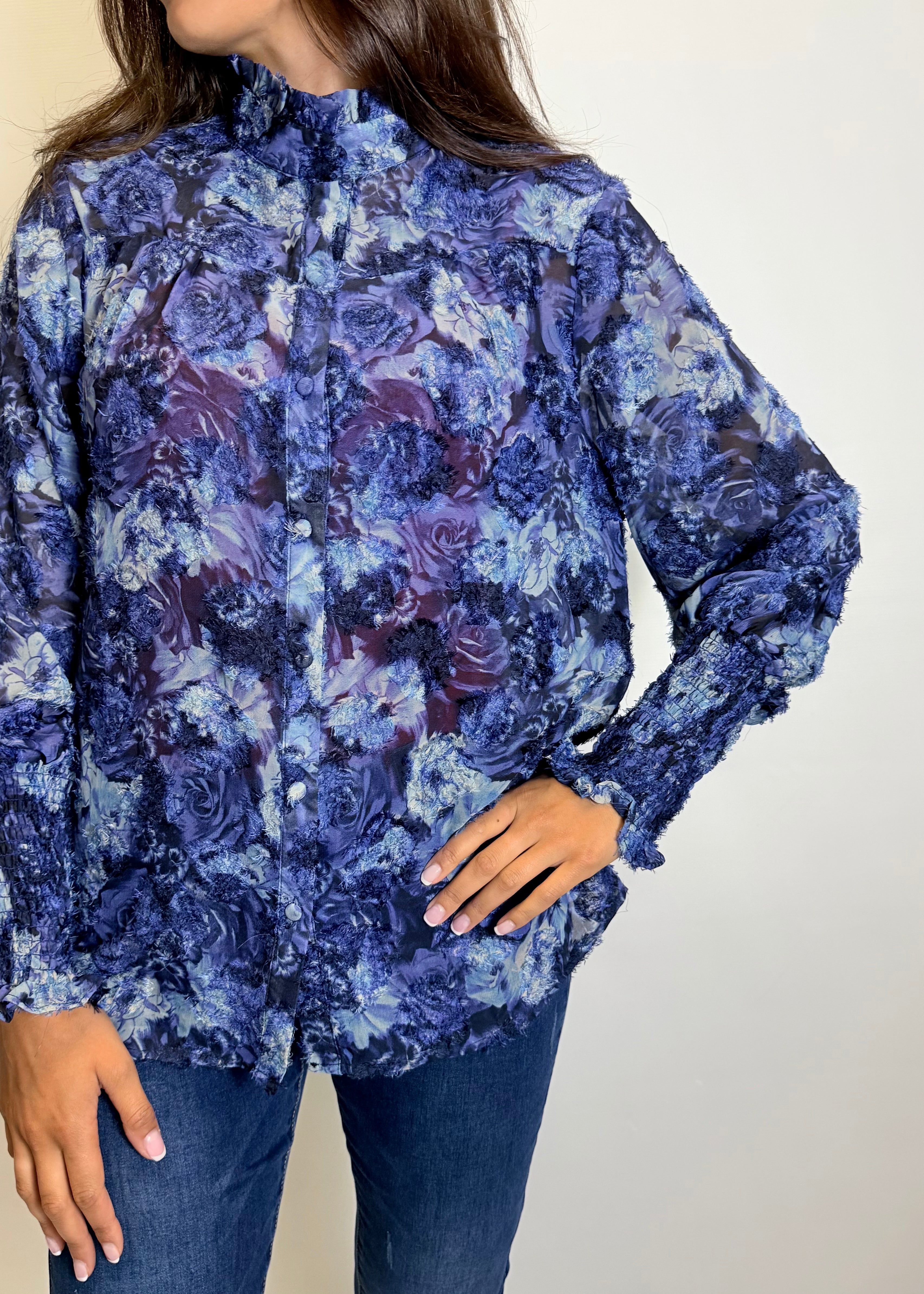 Woman wearing a blue floral blouse, jeans, and brown boots against a plain background