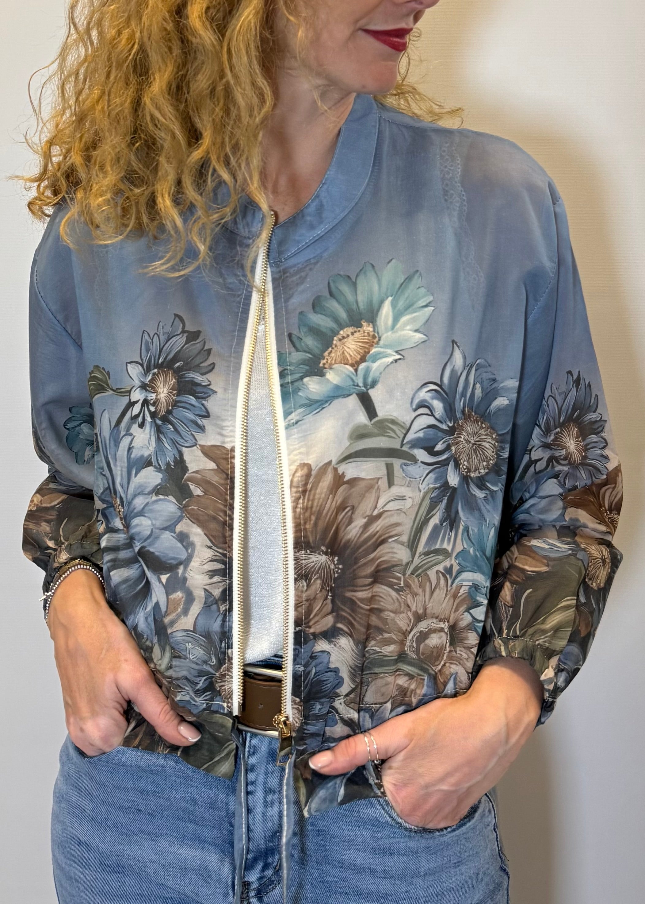 Woman wearing a floral-patterned bomber jacket against a plain background