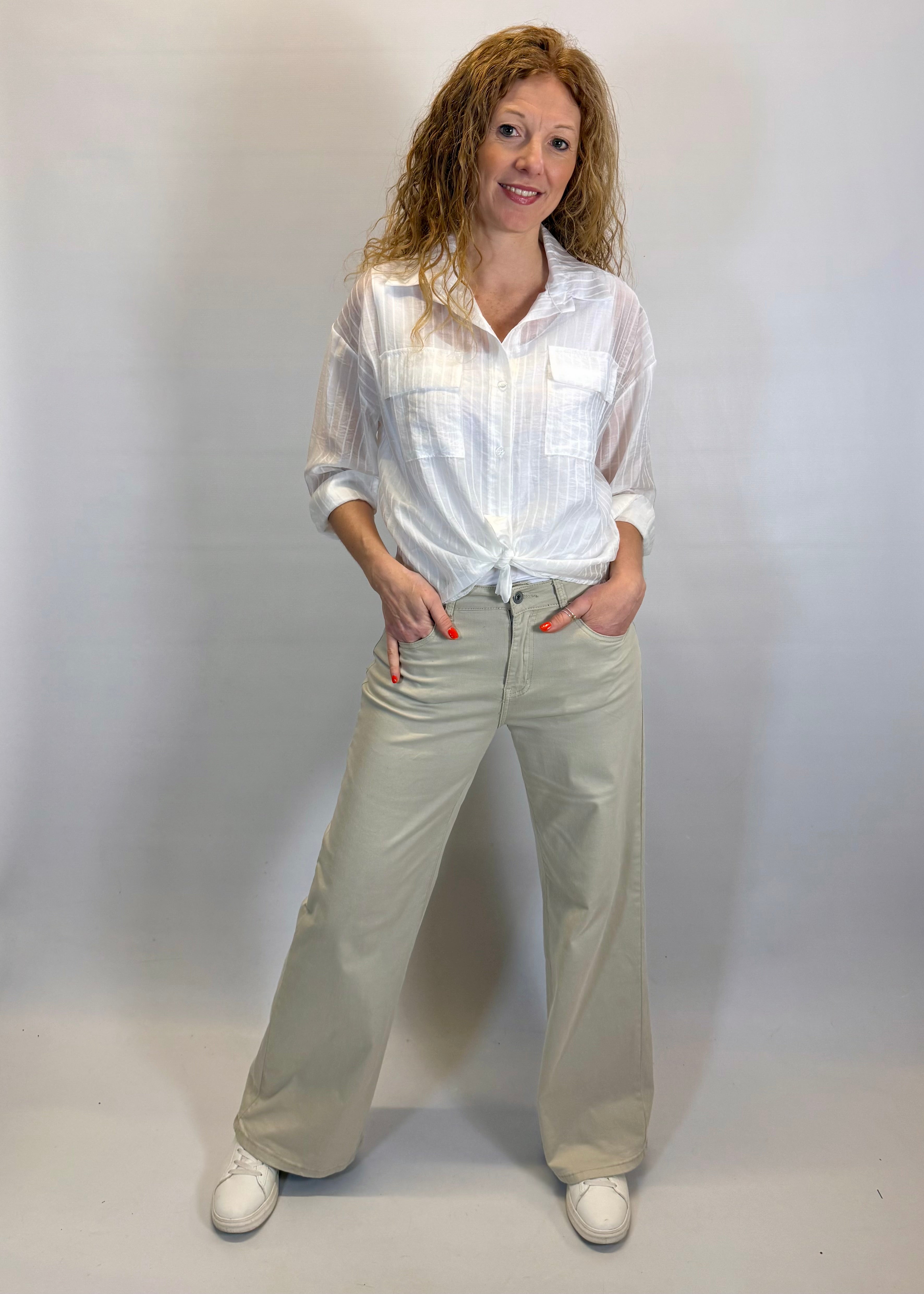 Woman wearing a white shirt and beige pants against a plain background