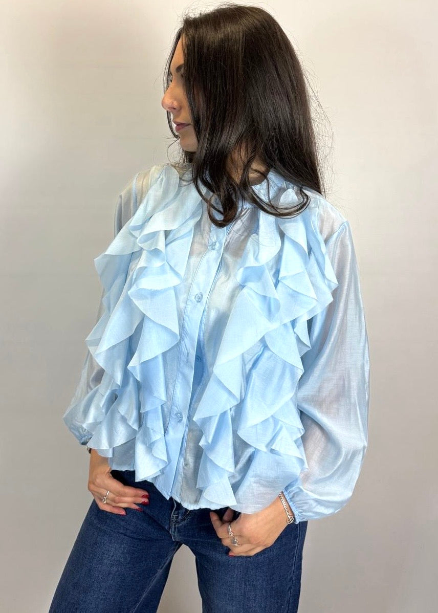 Woman wearing a light blue ruffled blouse against a plain background