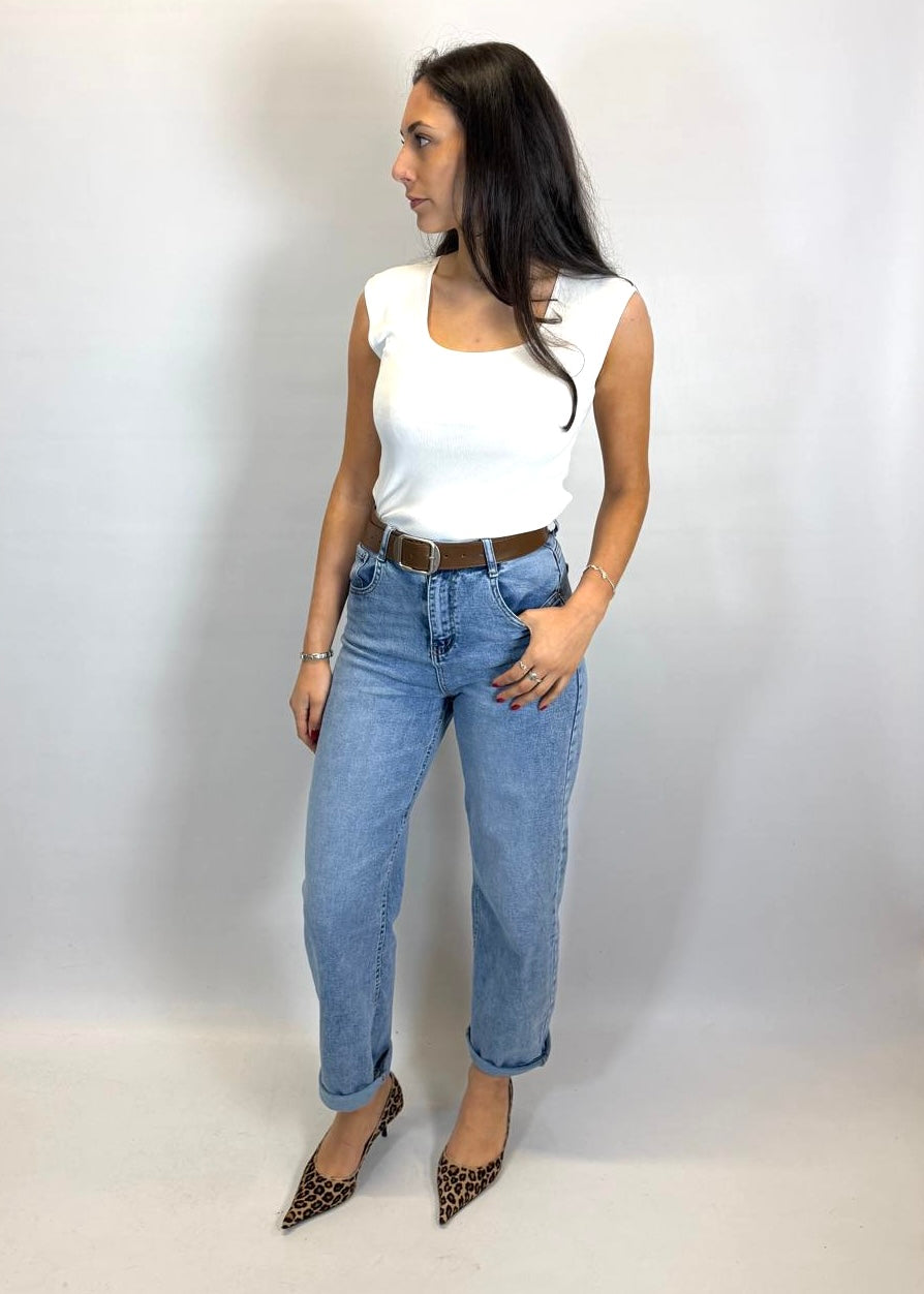 Woman wearing a white top and blue jeans against a plain background