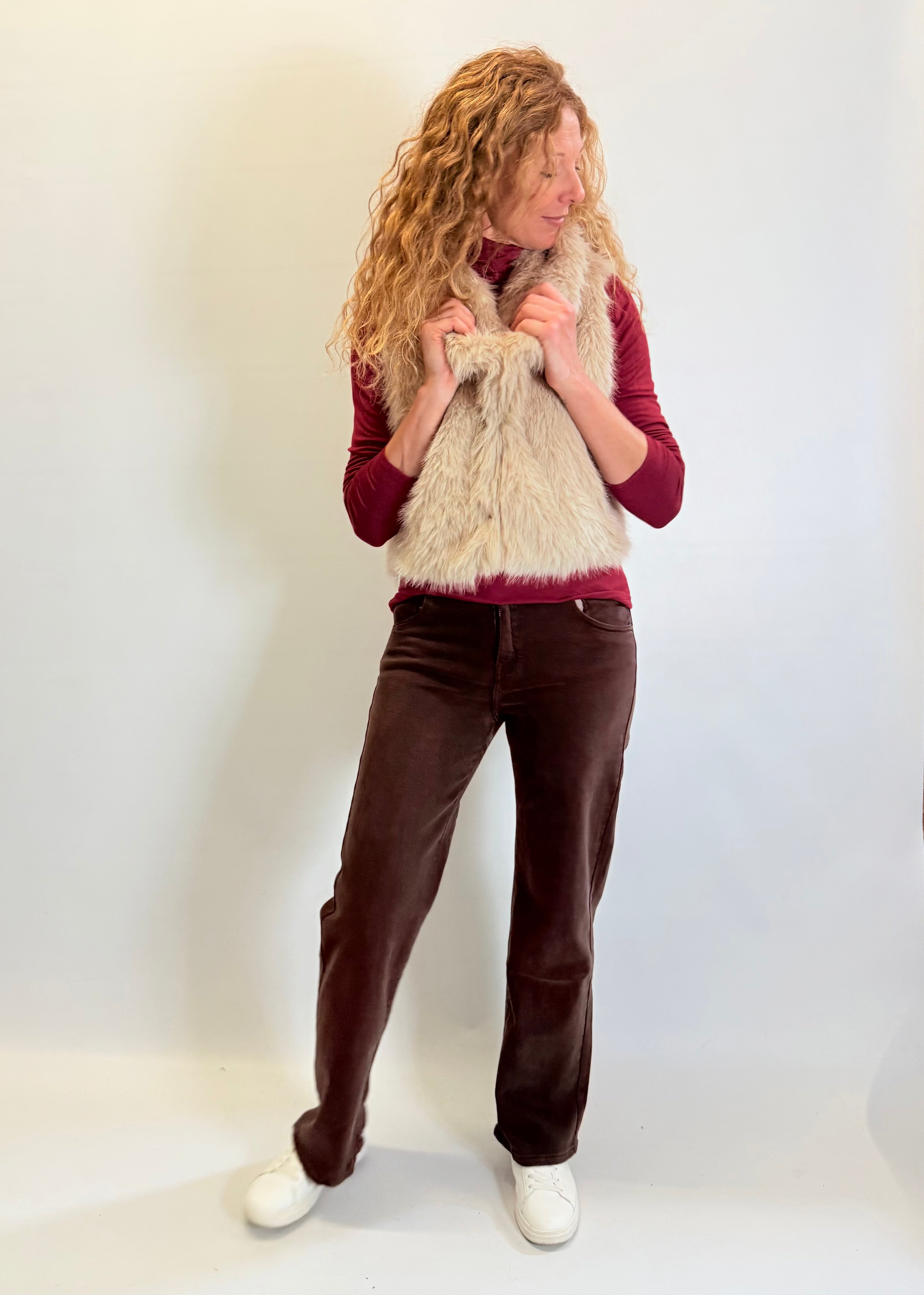 Person wearing a red sweater, brown pants, and a beige scarf against a white background