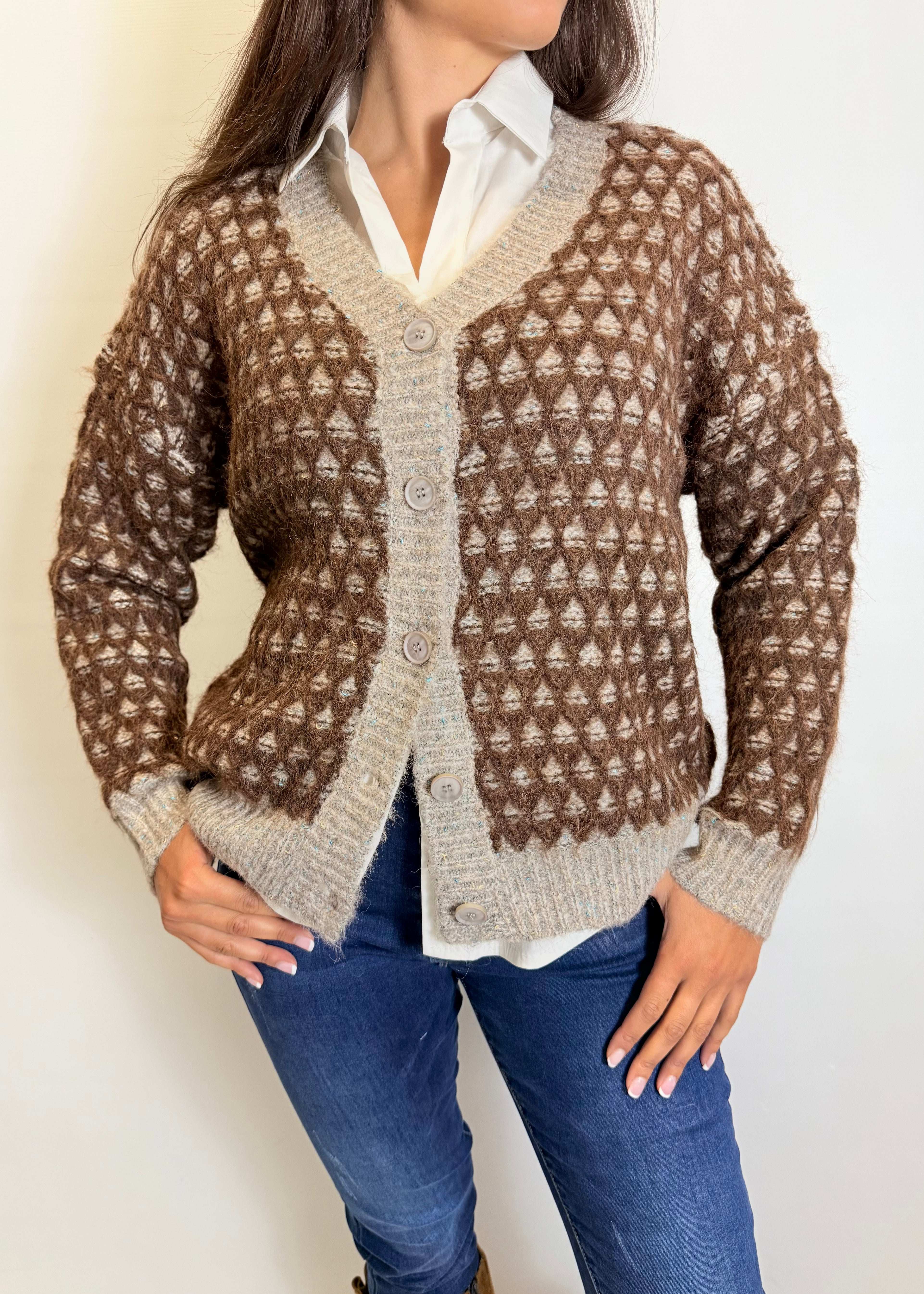 Person wearing a brown and beige patterned cardigan over a white shirt and blue jeans on a plain background
