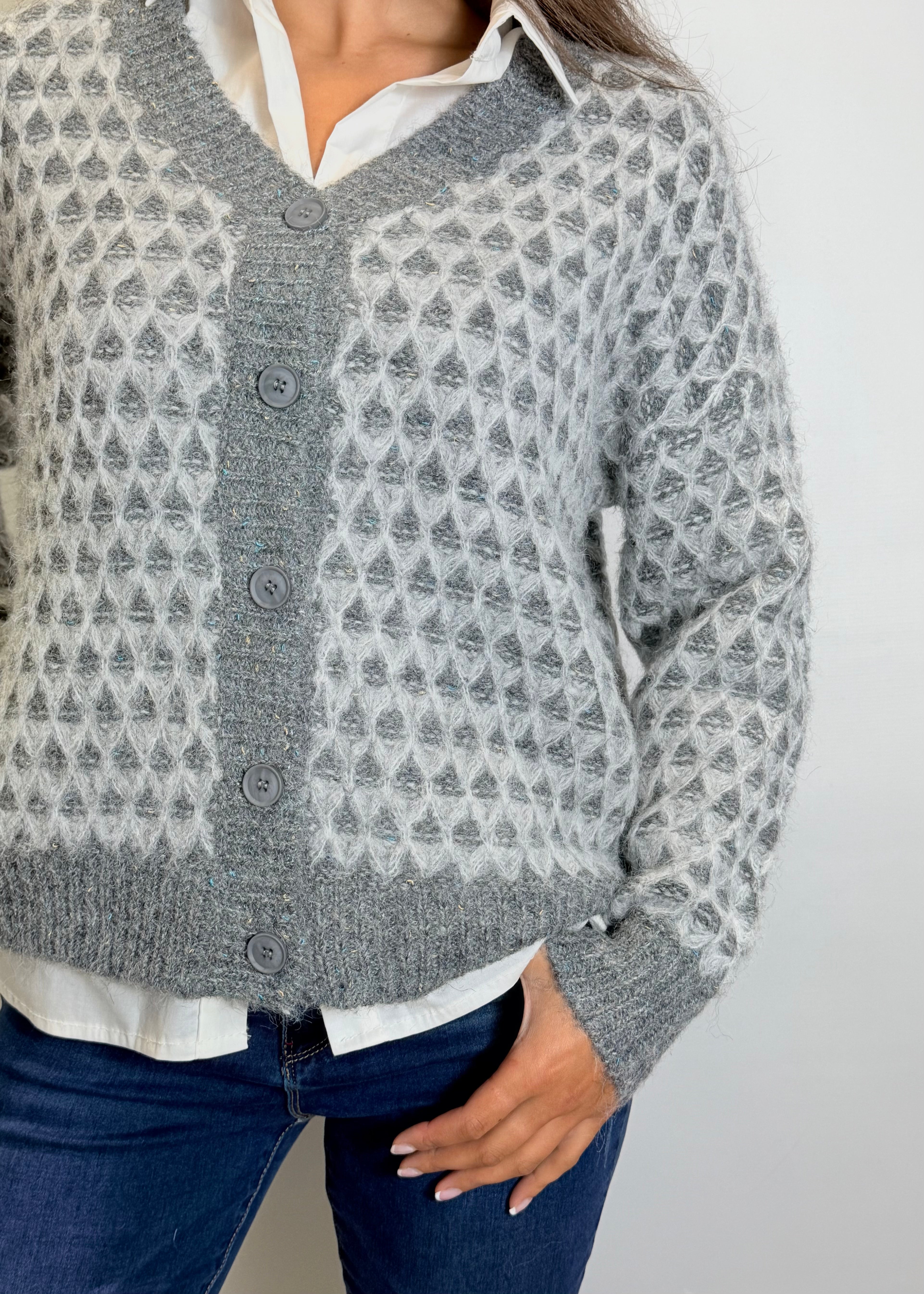 Person wearing a patterned gray cardigan over a white shirt with a plain background
