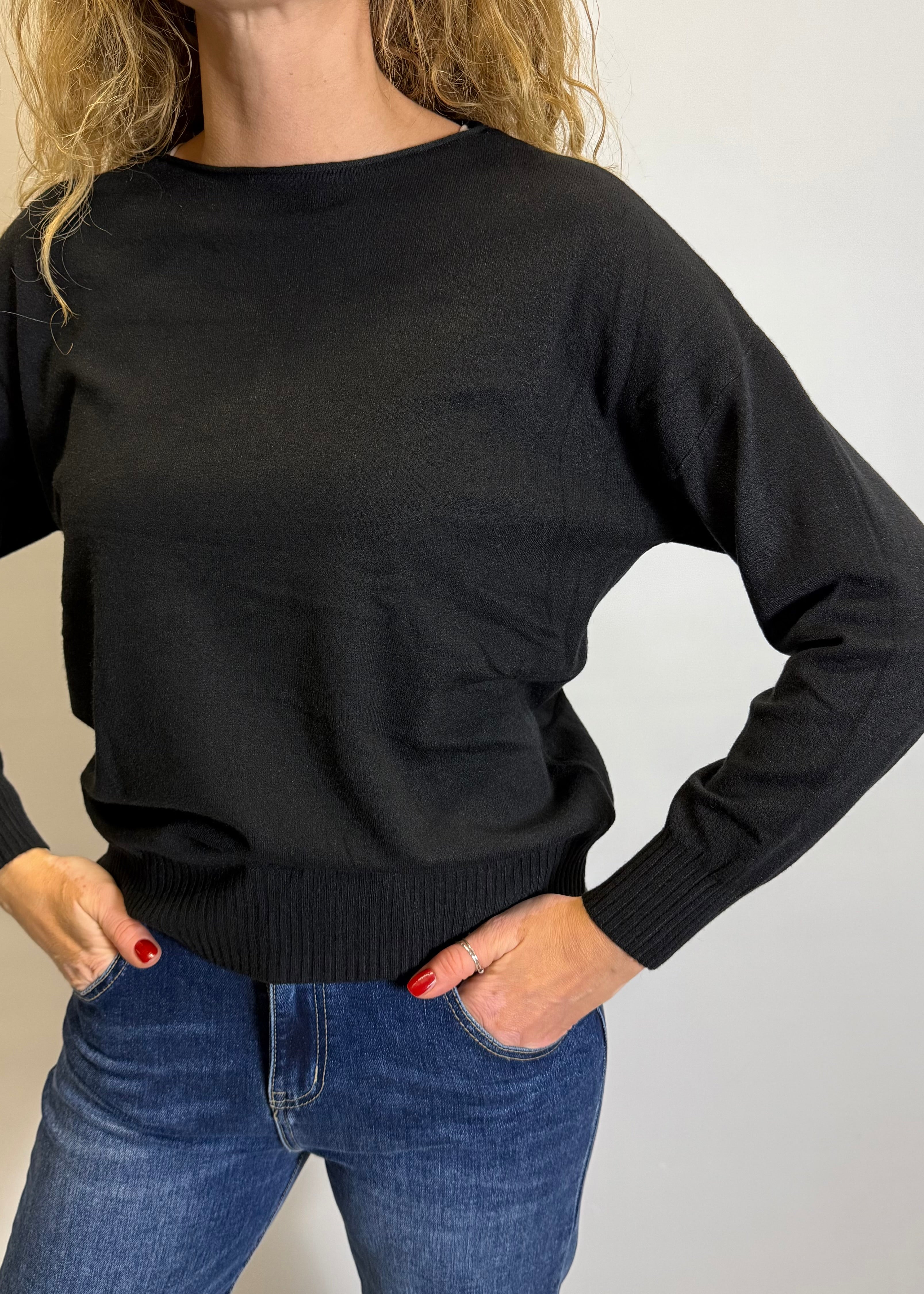 Person wearing a black sweater and blue jeans on a plain background