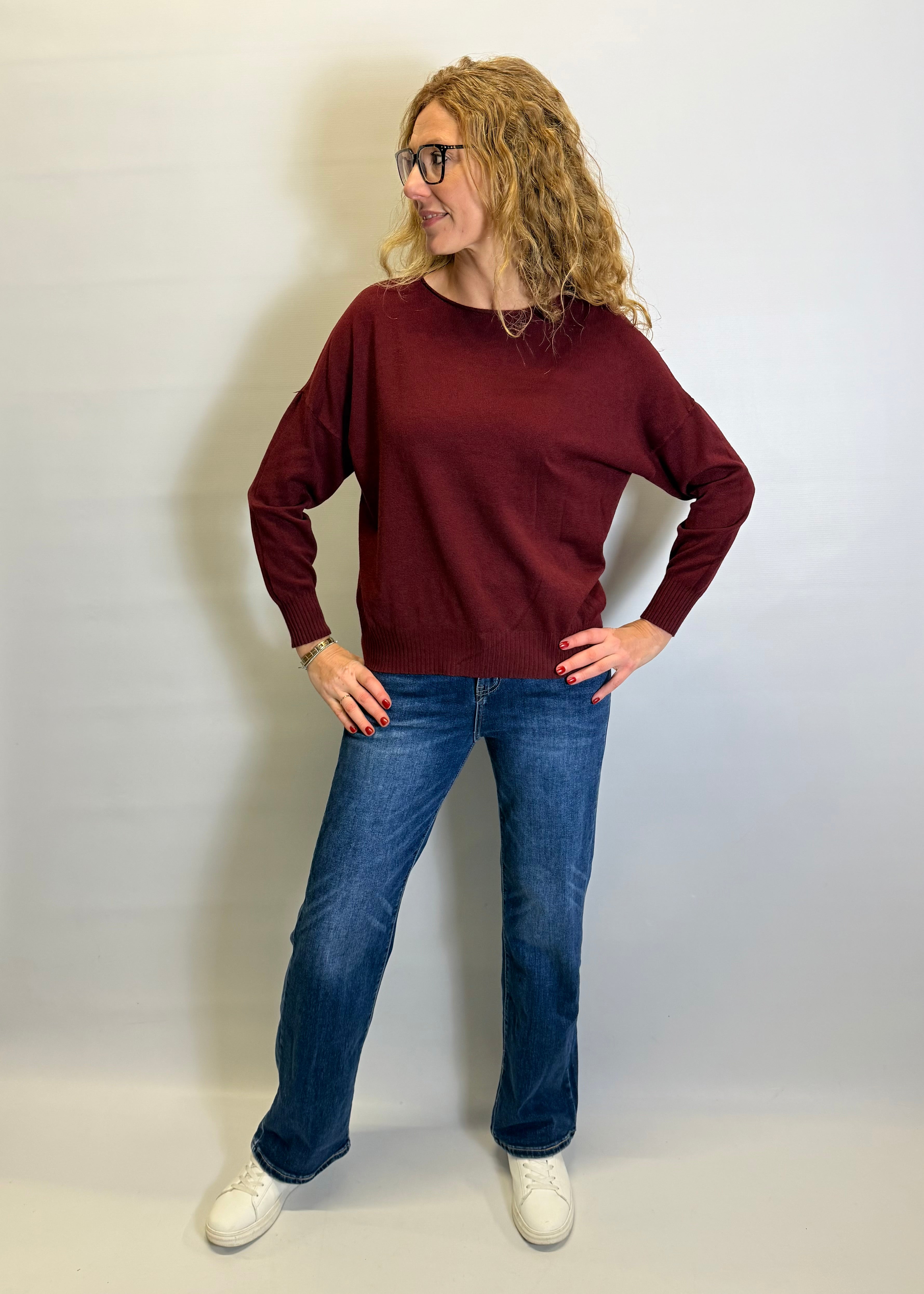 Woman wearing a burgundy sweater and blue jeans against a white background