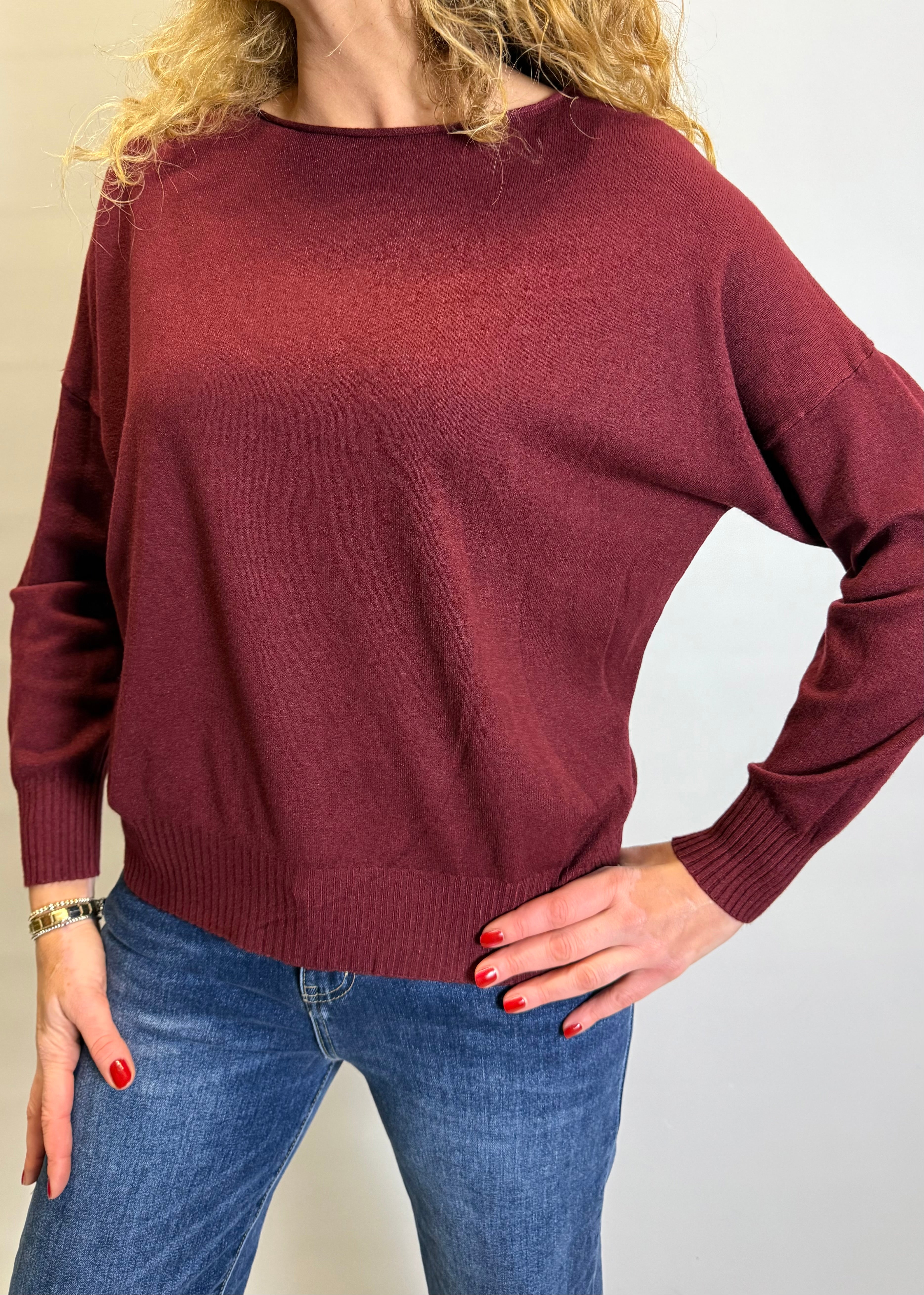 Person wearing a burgundy sweater and blue jeans against a plain background