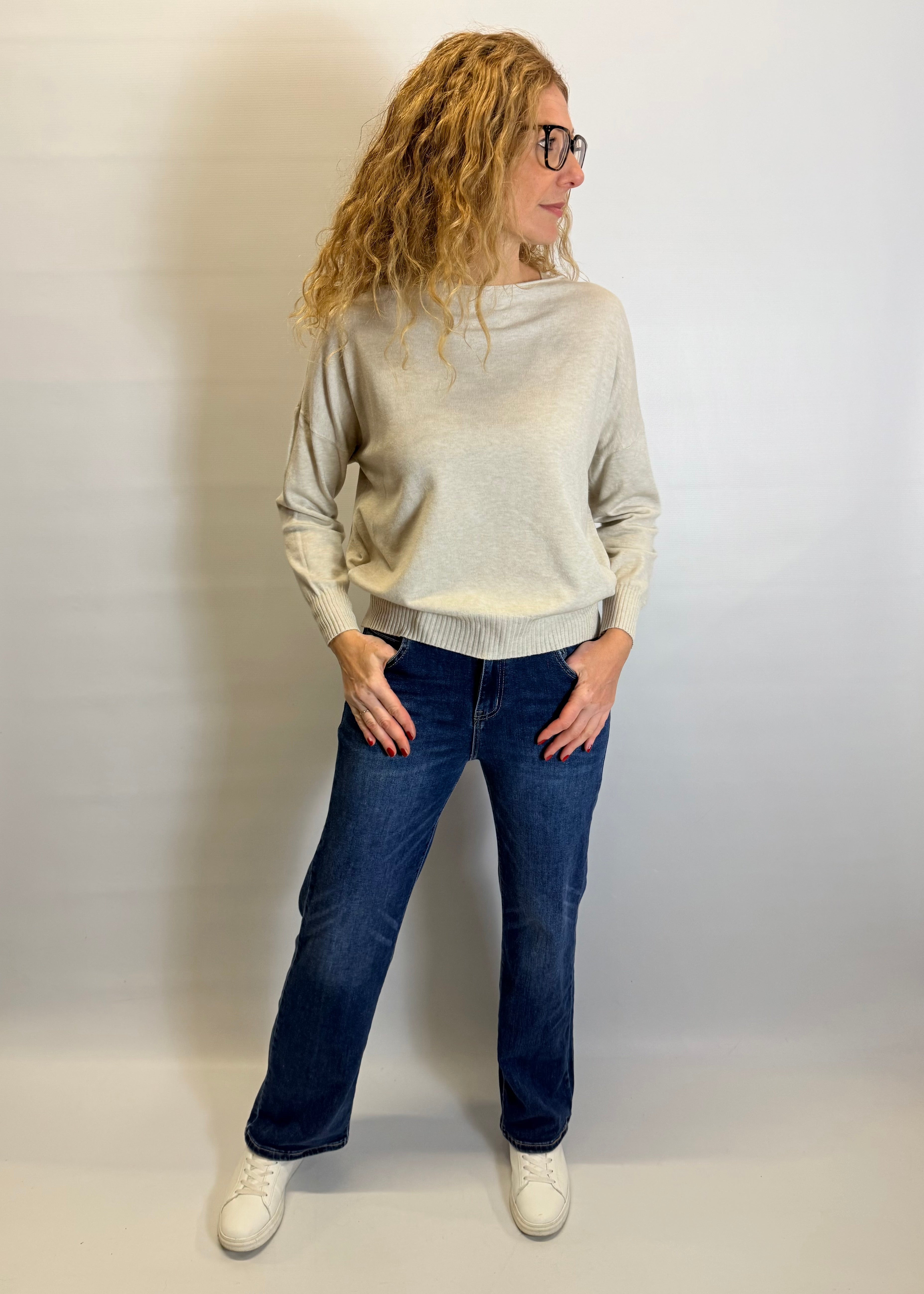 Person wearing a beige sweater and blue jeans against a plain background