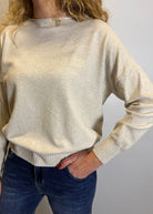 Person wearing a beige sweater and blue jeans against a plain background