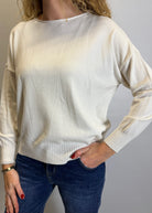 Person wearing a cream sweater and blue jeans against a plain background