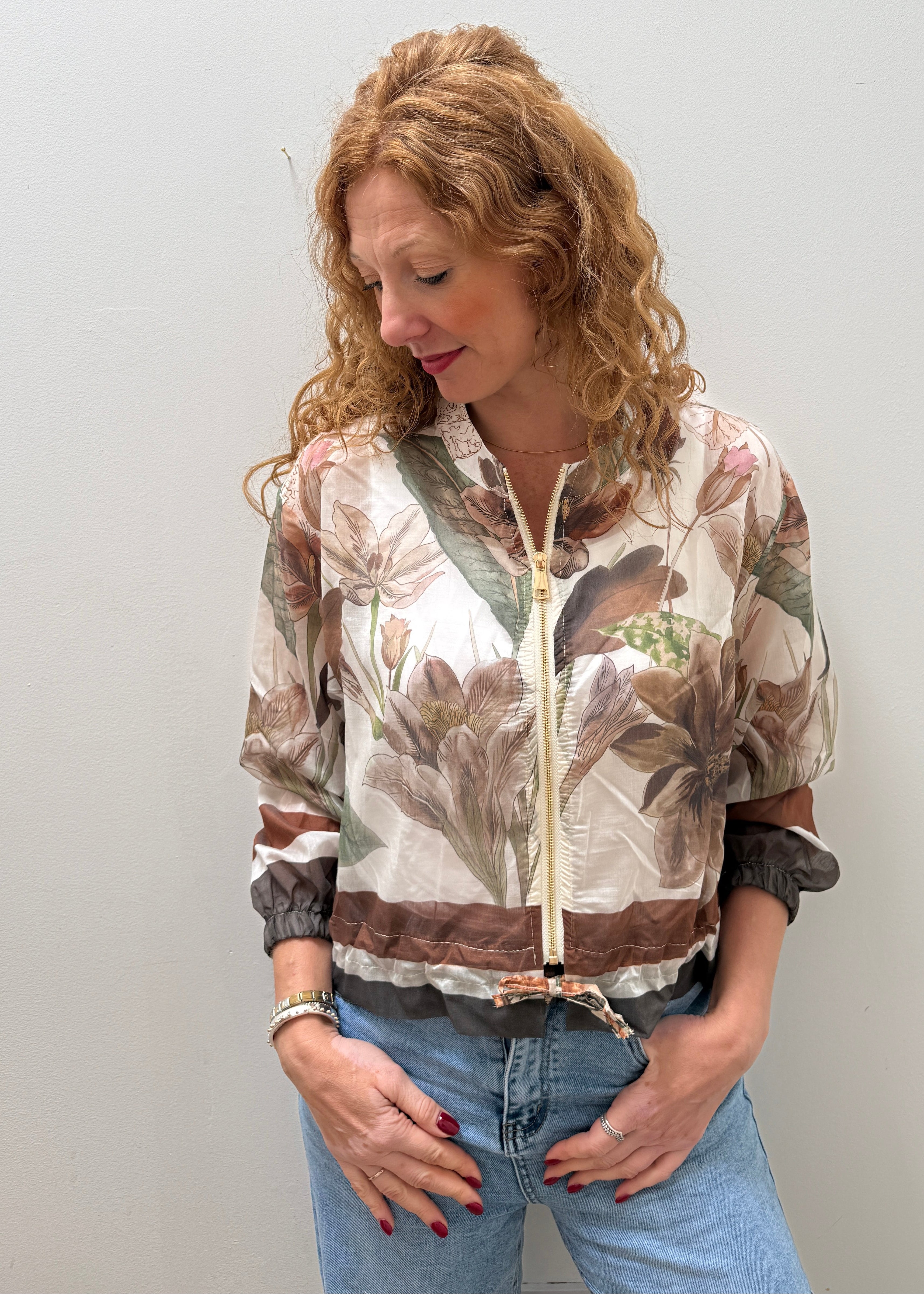 Person wearing a patterned jacket and jeans on a plain background
