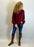 Person wearing a red sweater, blue jeans, and brown knee-high boots against a plain background