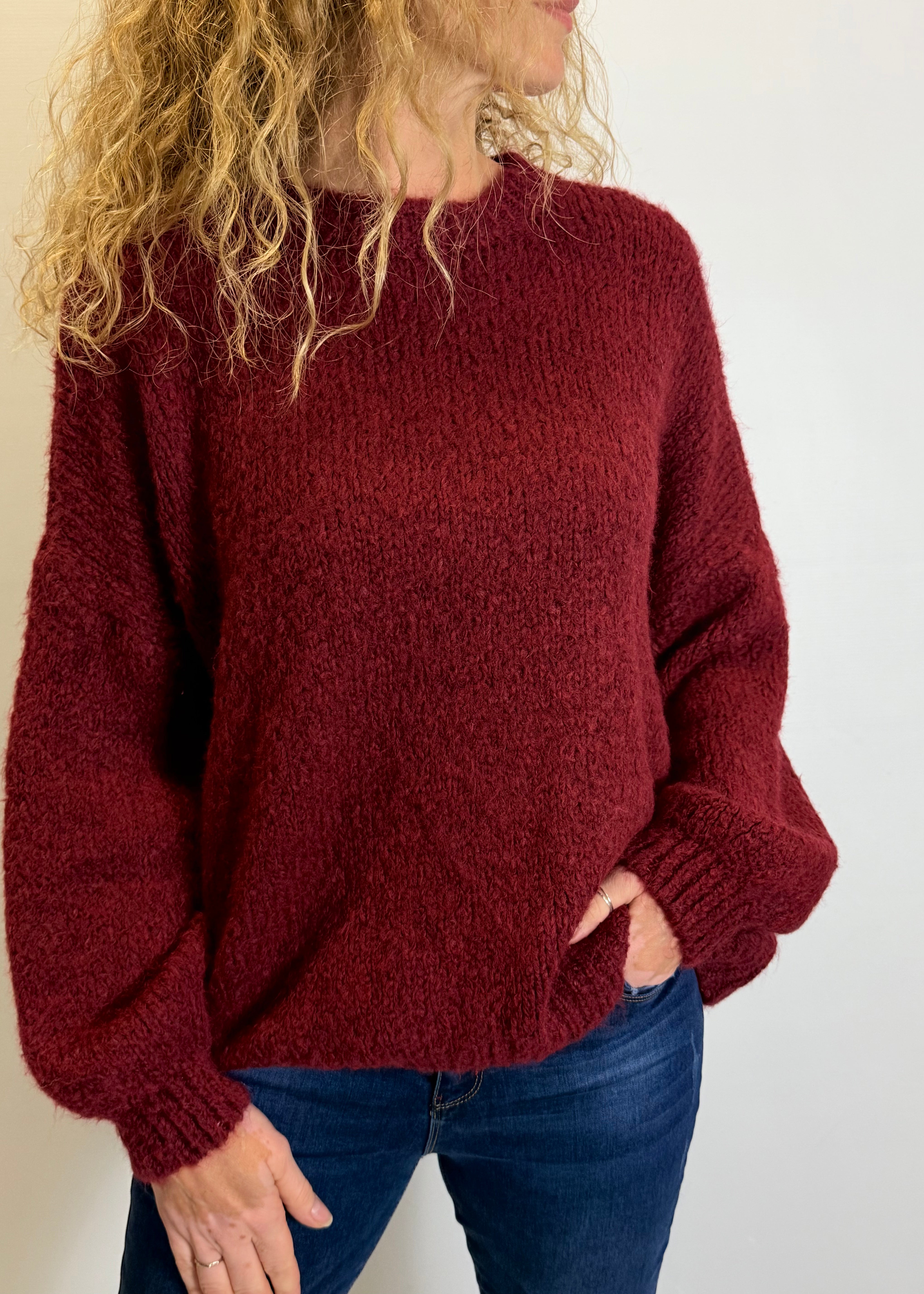 Person wearing a red sweater and blue jeans against a plain background