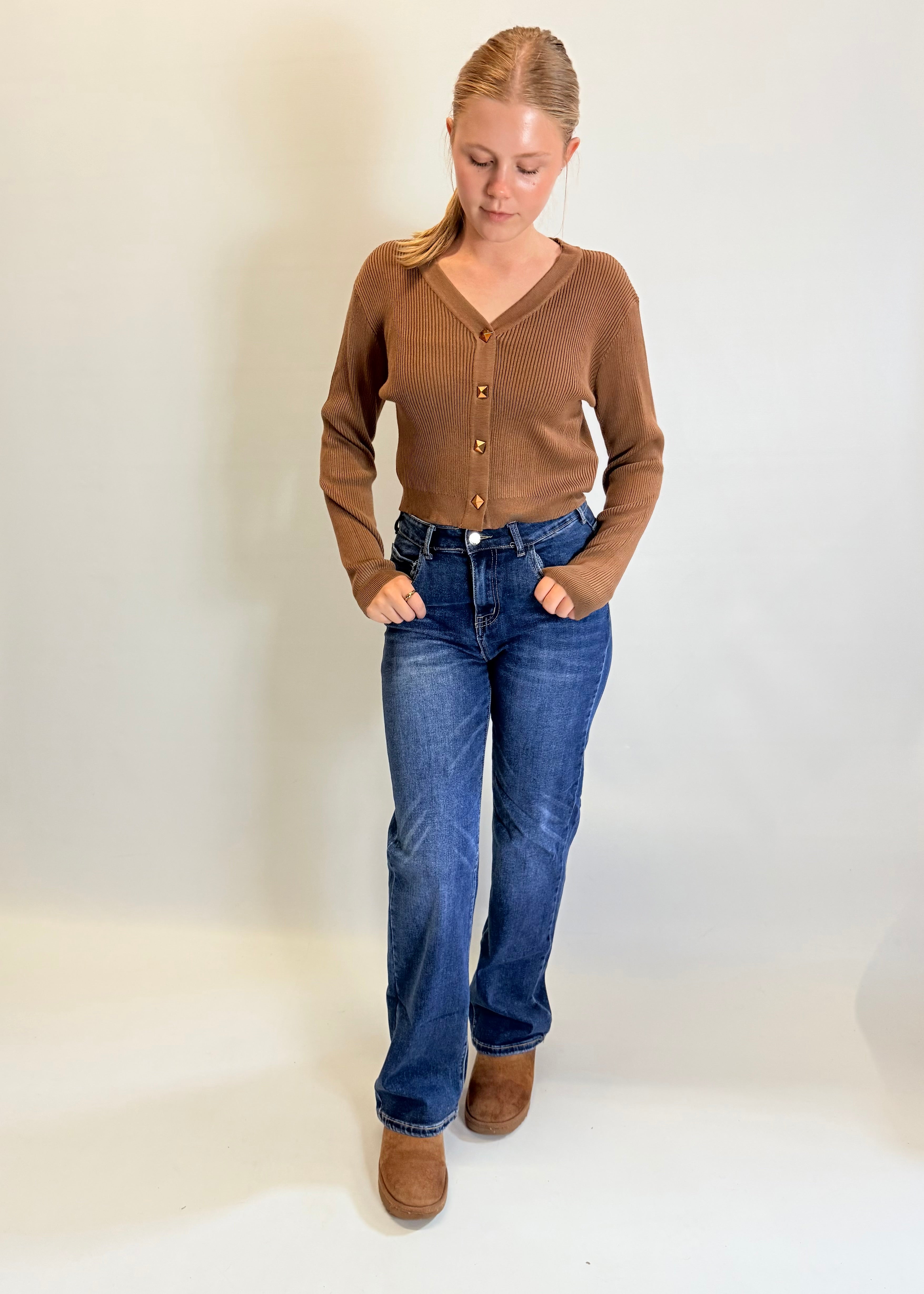 Woman wearing a brown cardigan, blue jeans, and brown boots on a white background