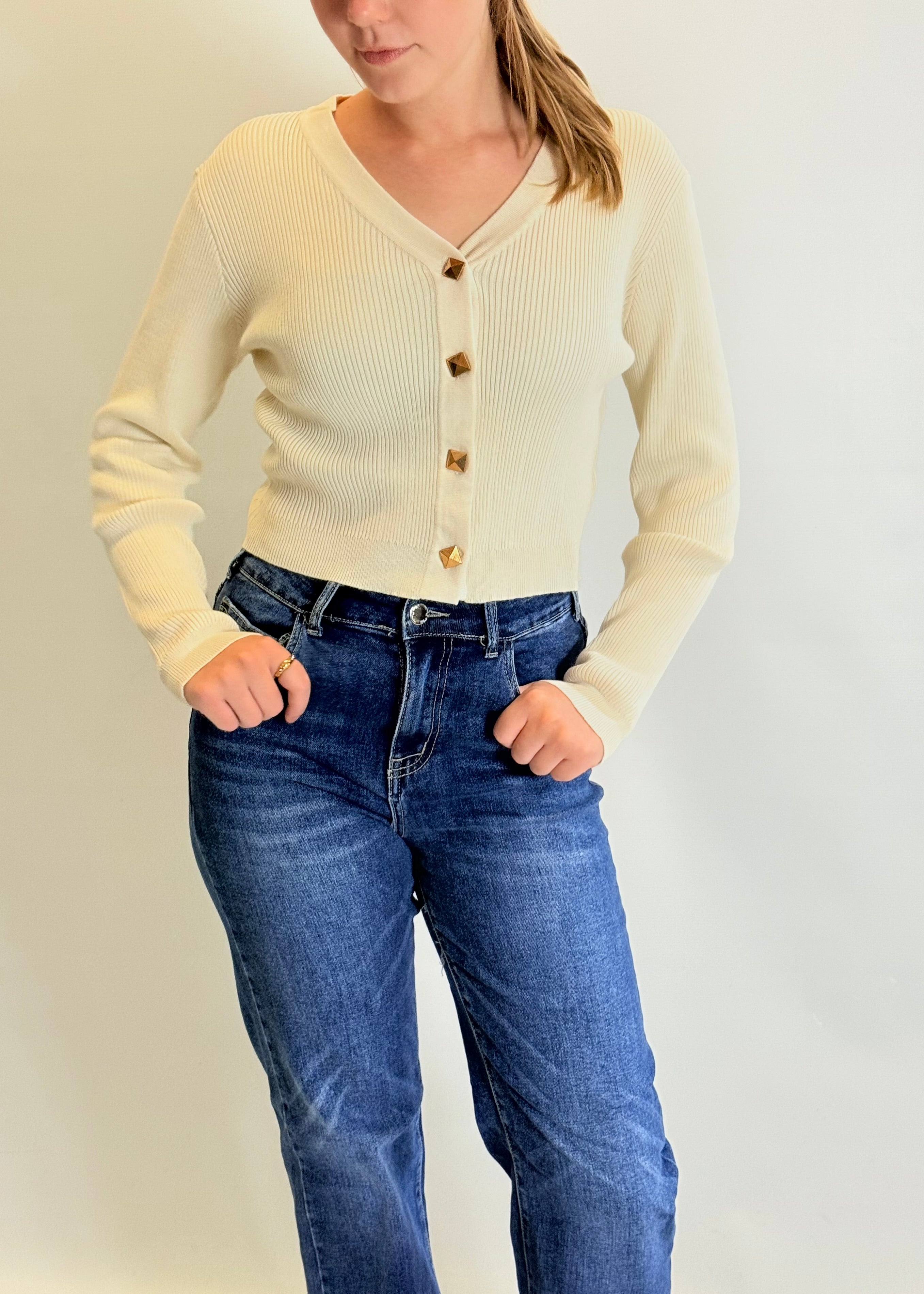 Person wearing a cream cardigan and blue jeans against a plain background