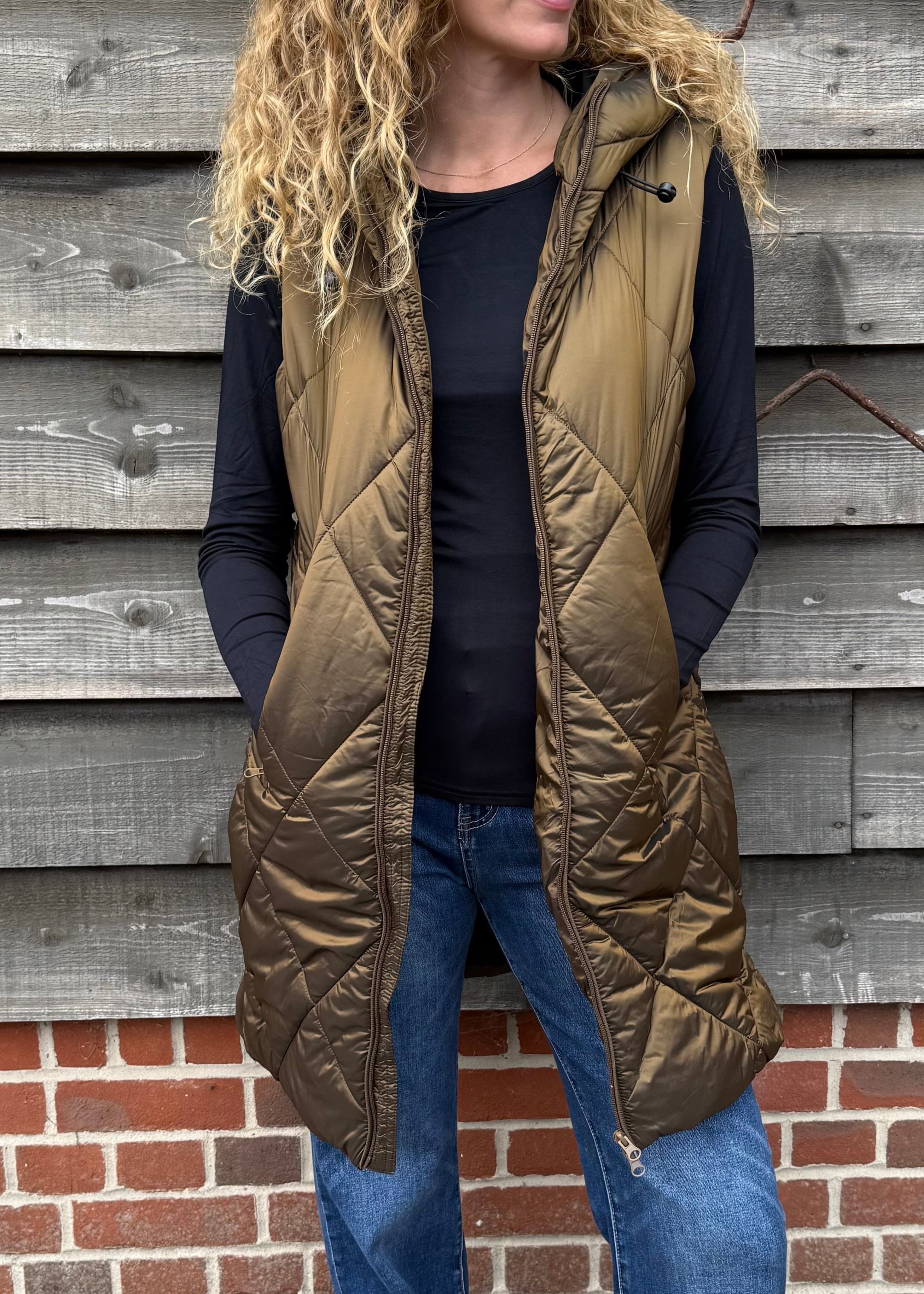 Woman wearing a green puffer vest standing against a wooden wall.