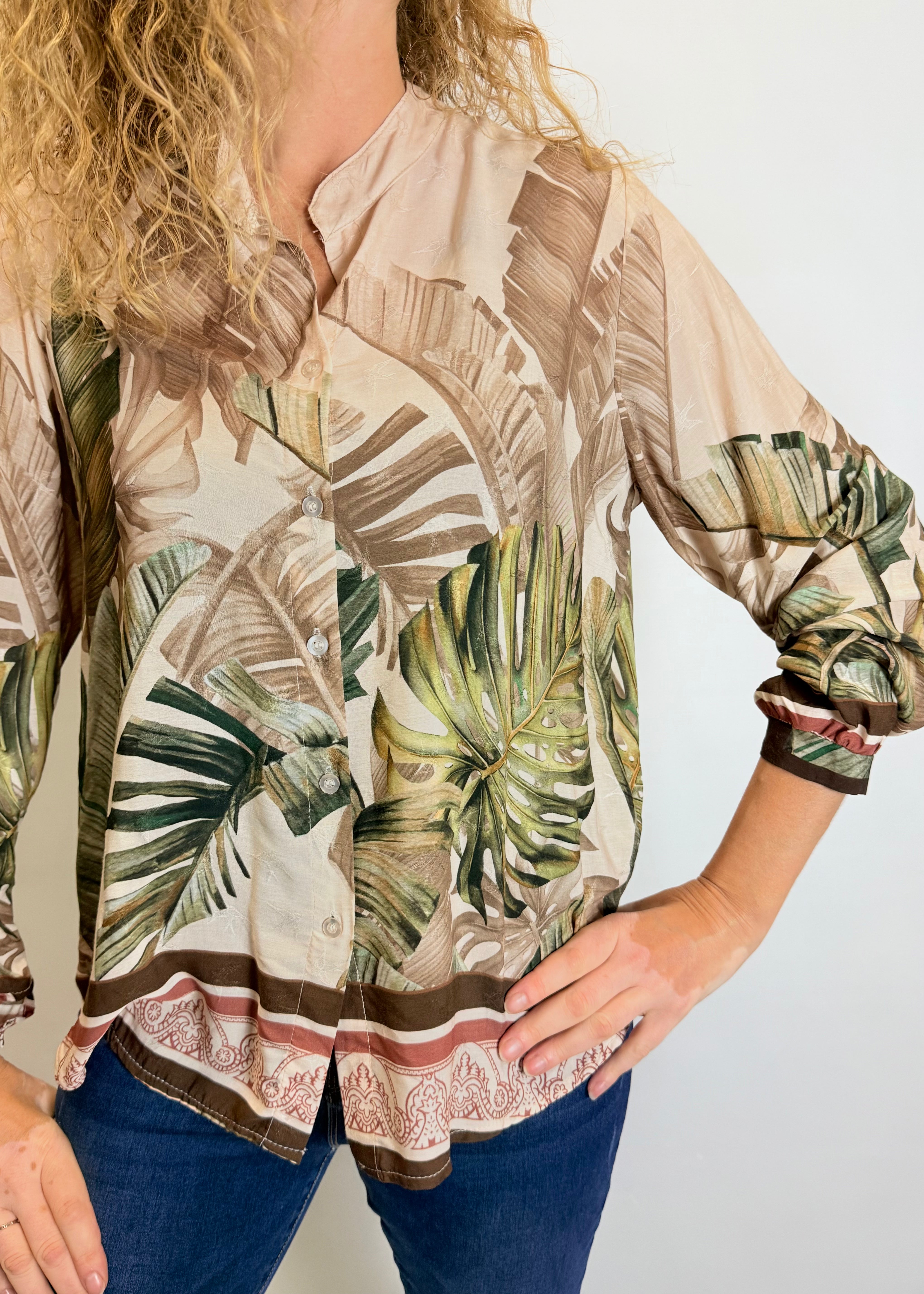 Woman wearing a tropical leaf patterned blouse with rolled-up sleeves against a plain background