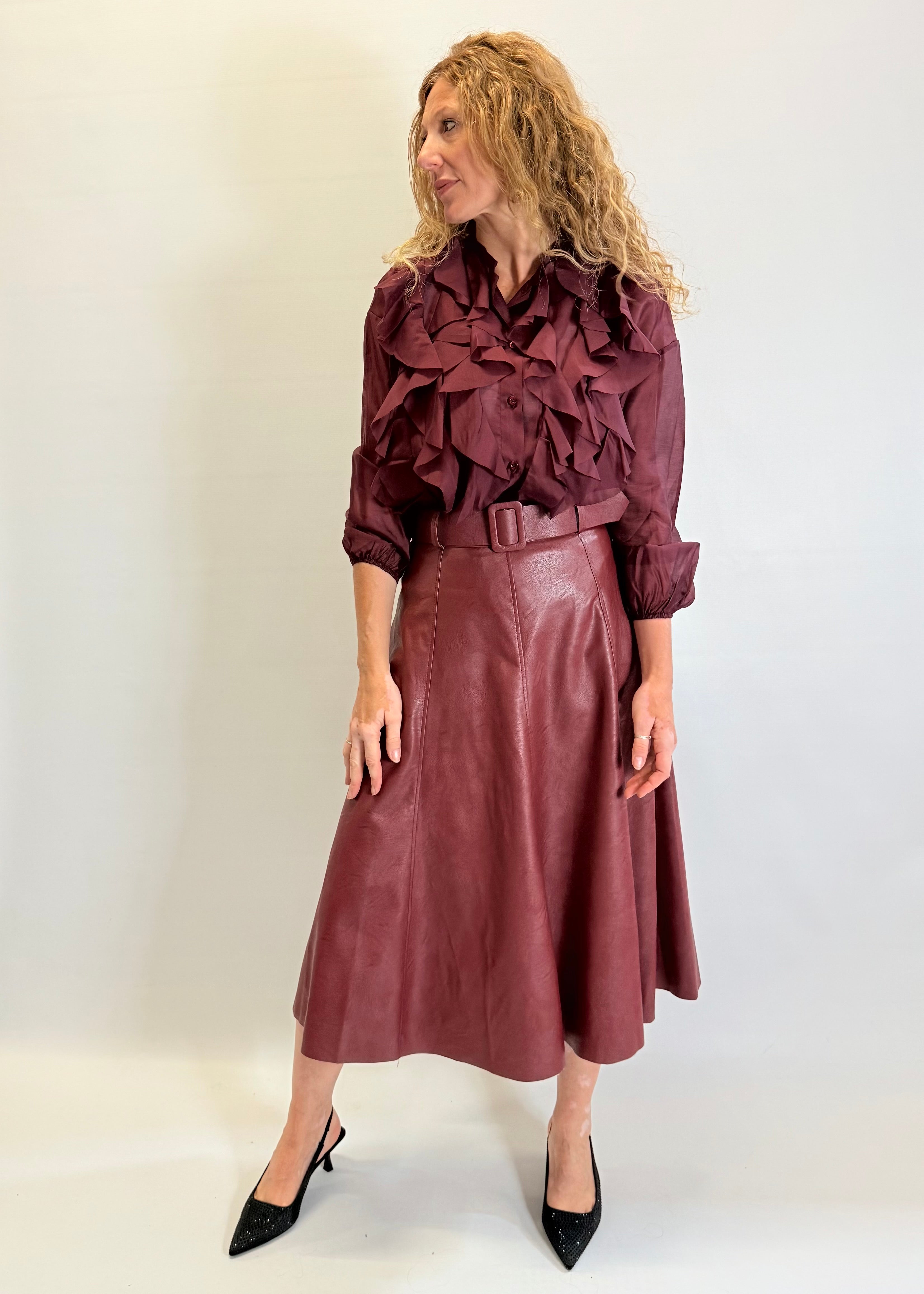 Woman wearing a burgundy ruffled blouse and leather skirt against a white background