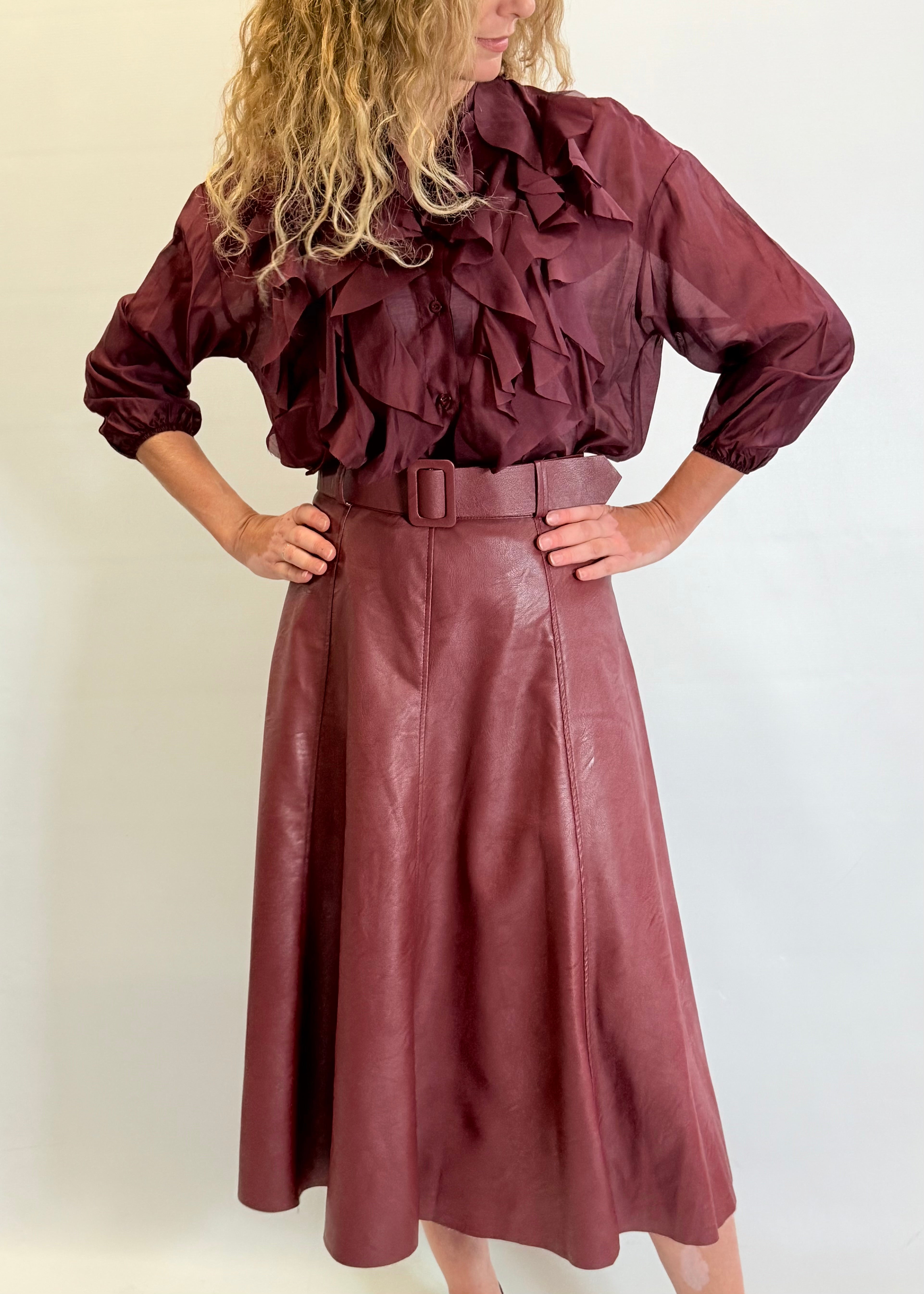 Person wearing a burgundy ruffled blouse and leather skirt against a plain background