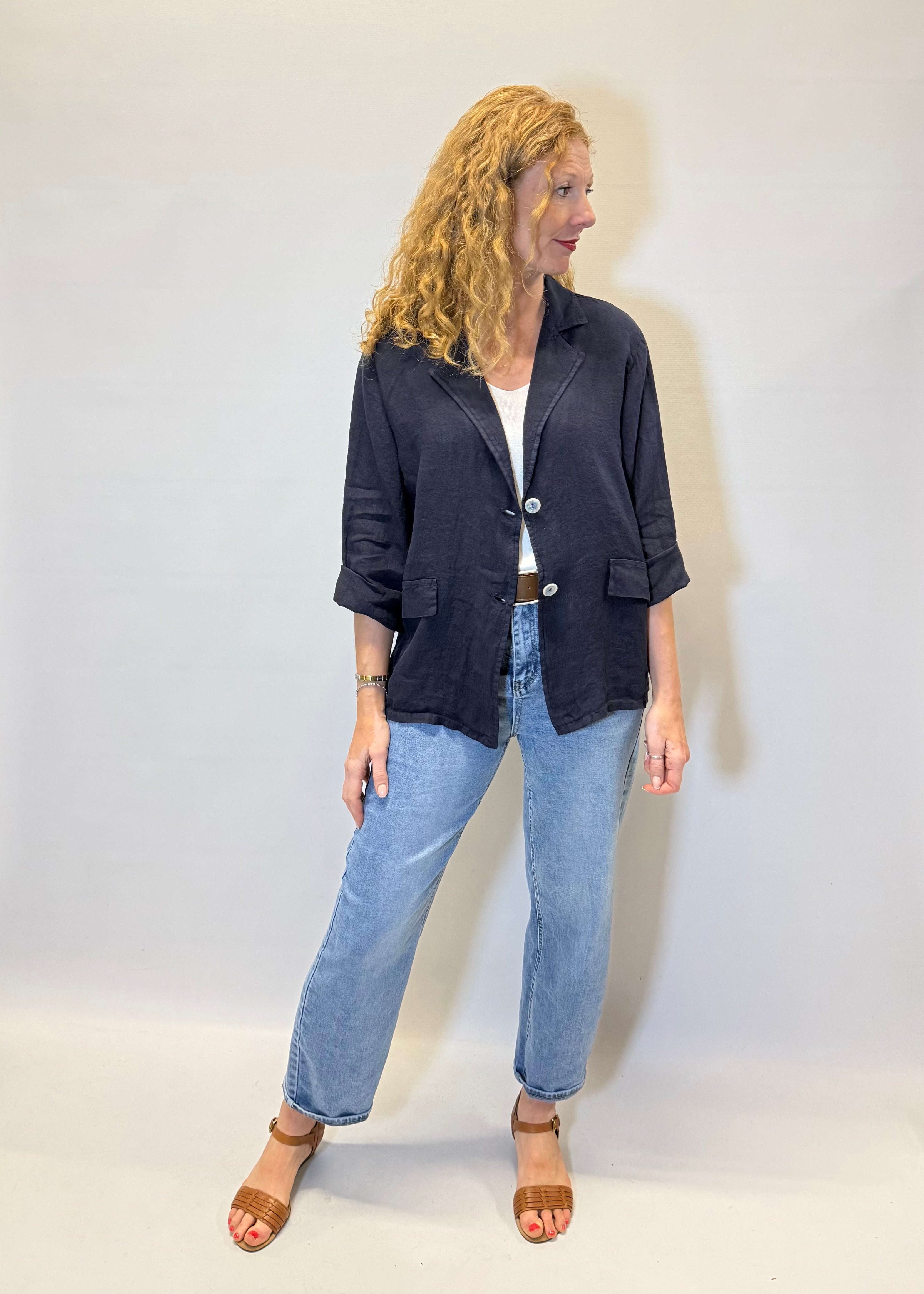 Woman wearing a dark jacket and light blue jeans against a white background