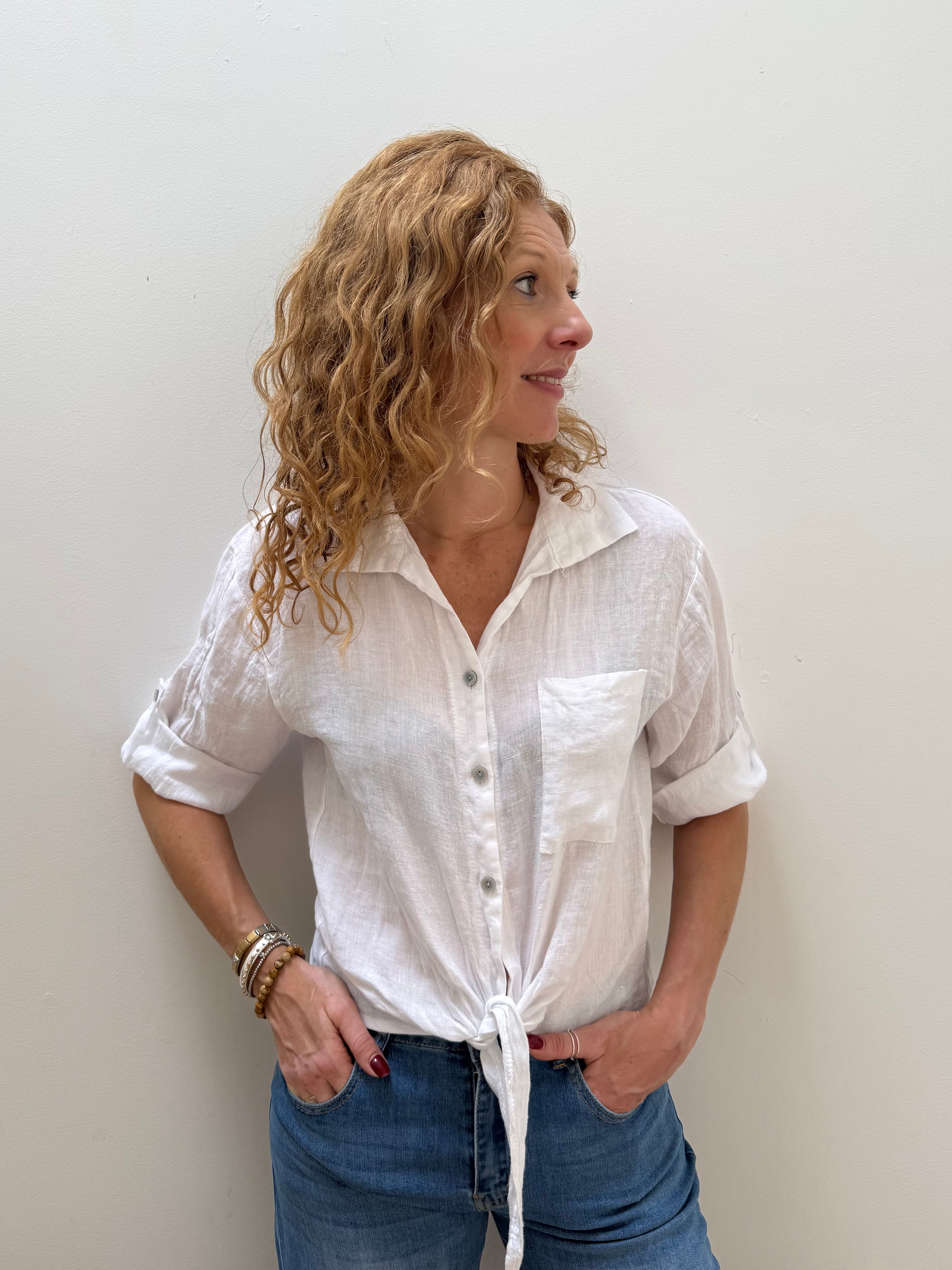 Woman wearing a white button-up shirt and blue jeans against a plain background