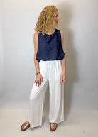 Person wearing a navy sleeveless top and white wide-leg pants against a plain background