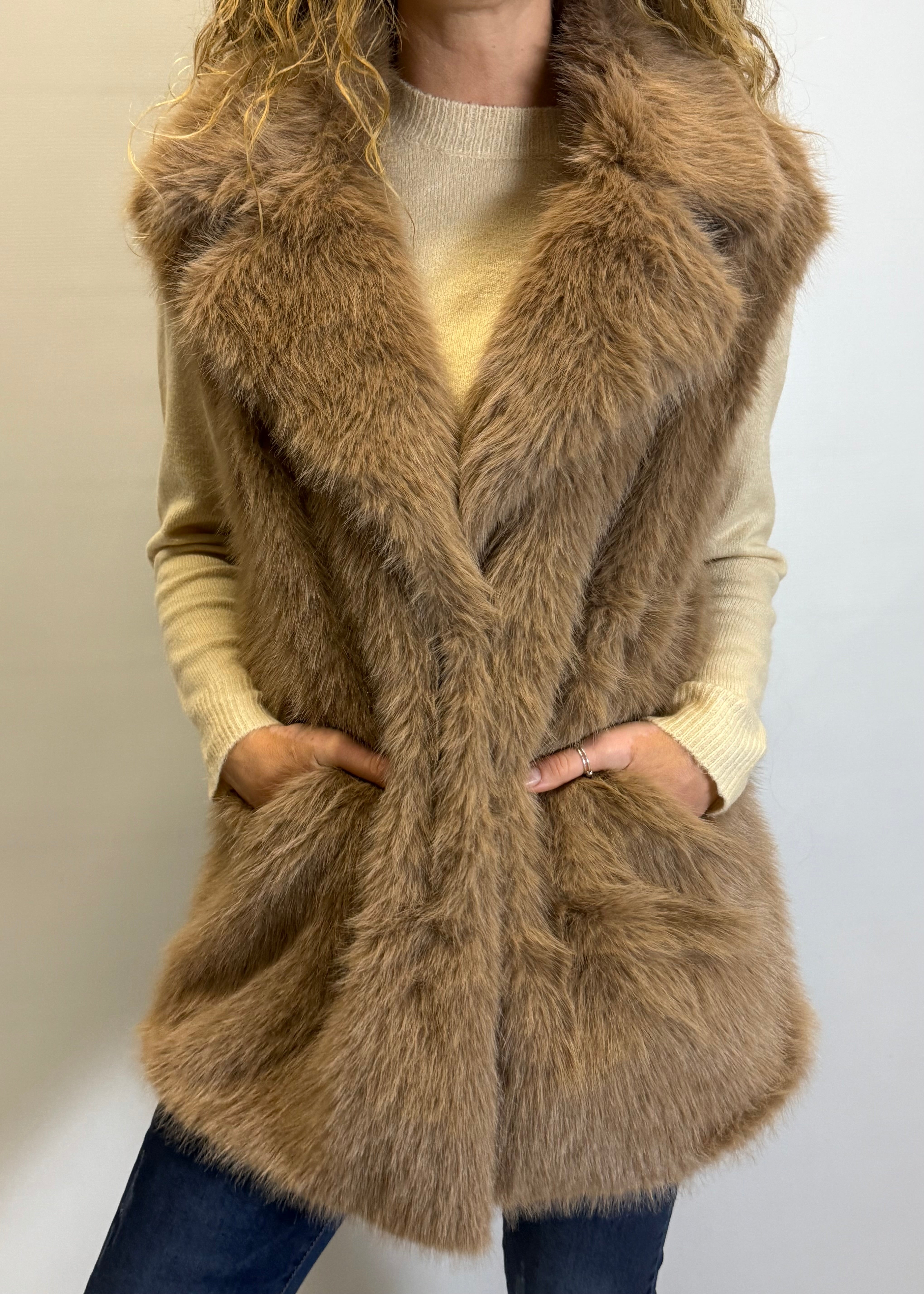 Person wearing a brown fur vest over a beige sweater on a plain background