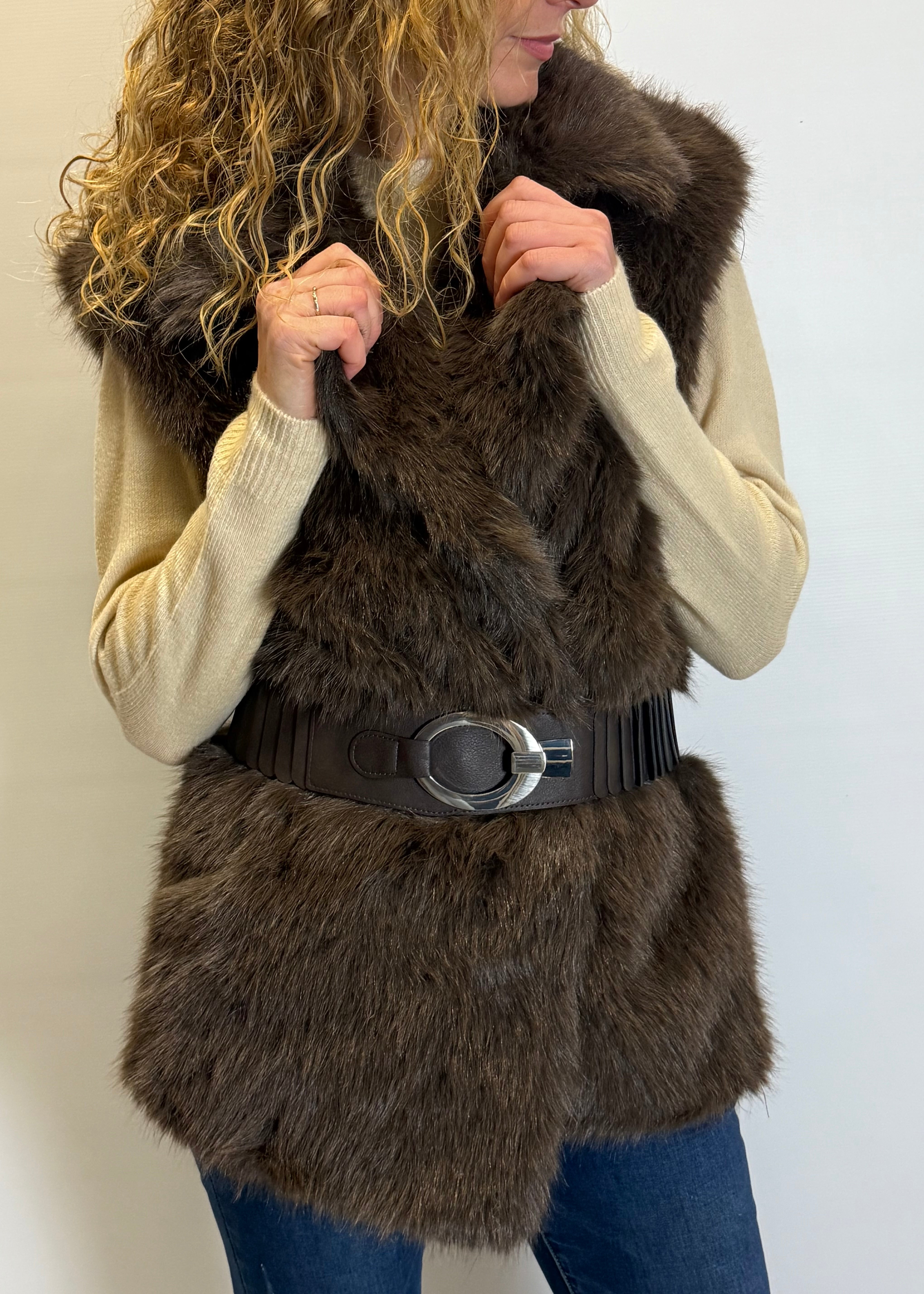 Person wearing a brown fur vest with a black belt against a white background