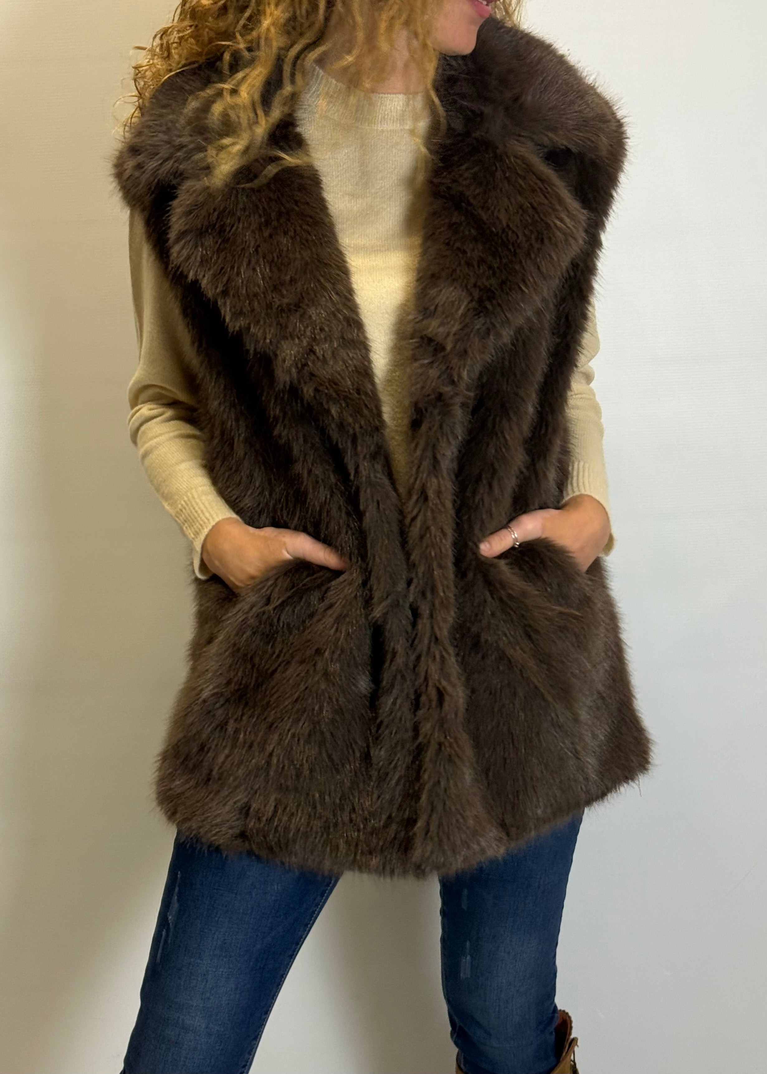 Person wearing a brown fur vest against a plain background