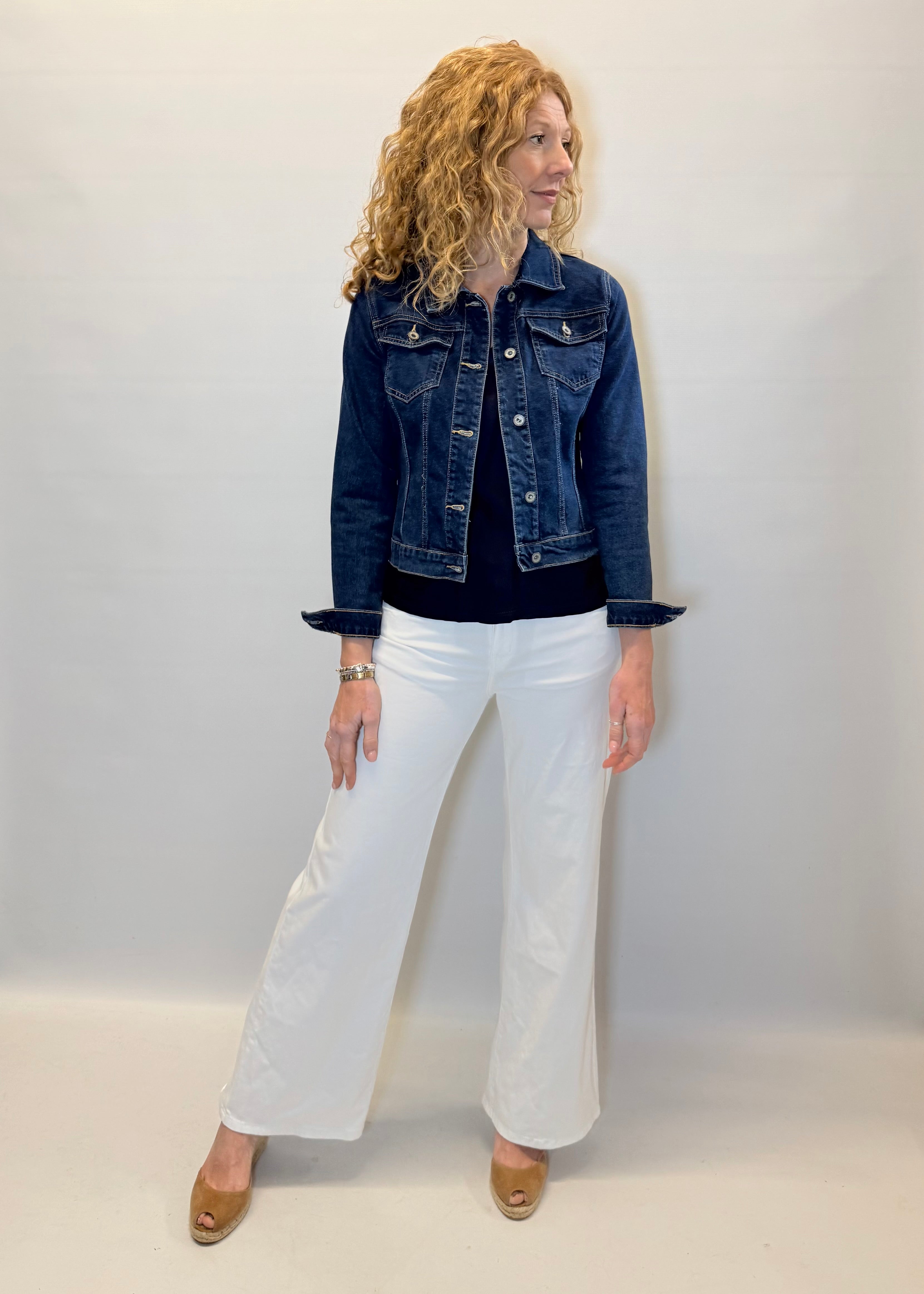 Woman wearing a denim jacket and white pants against a plain background