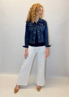 Woman wearing a denim jacket and white pants against a plain background