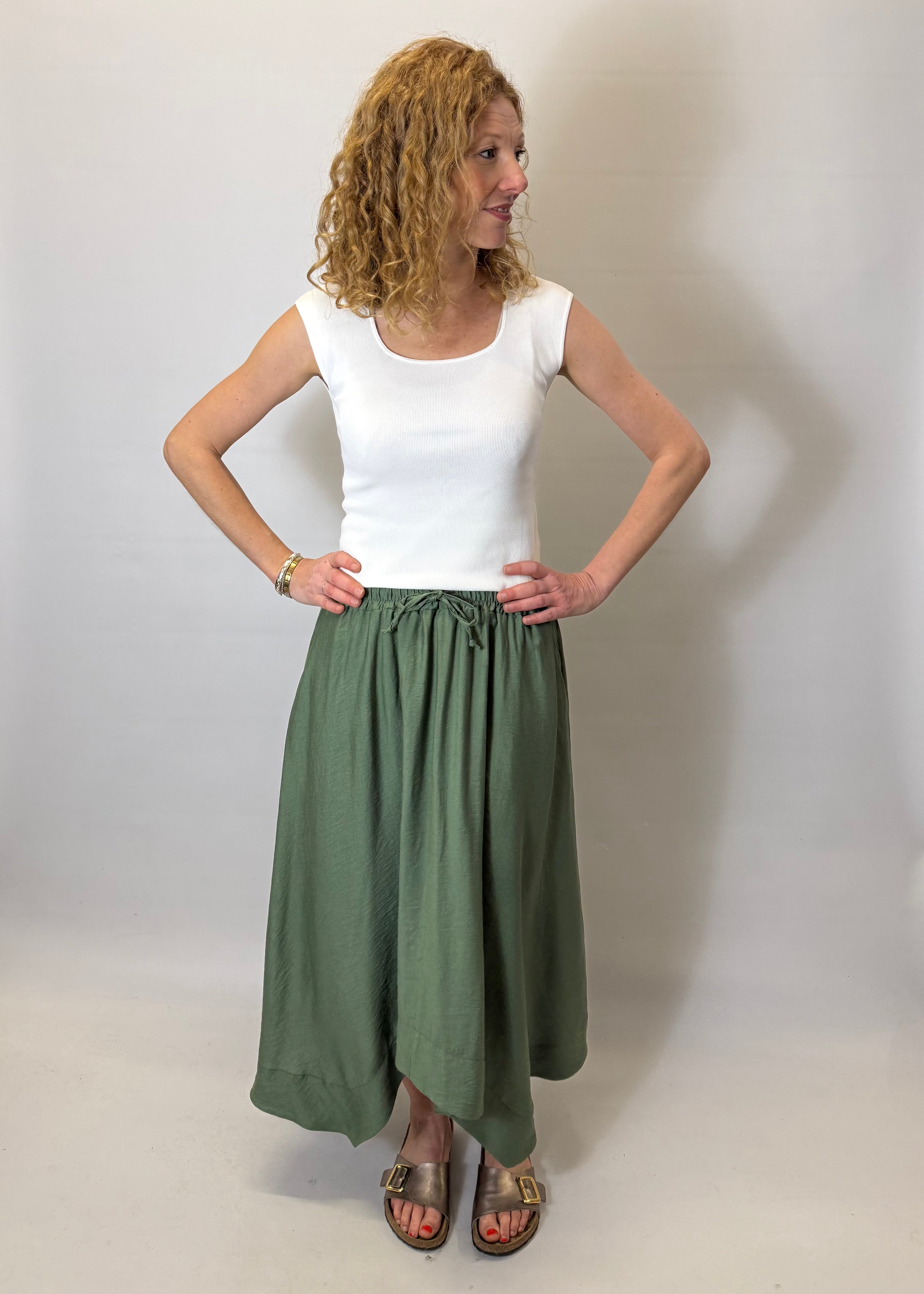 Woman wearing a white top and green skirt against a plain background