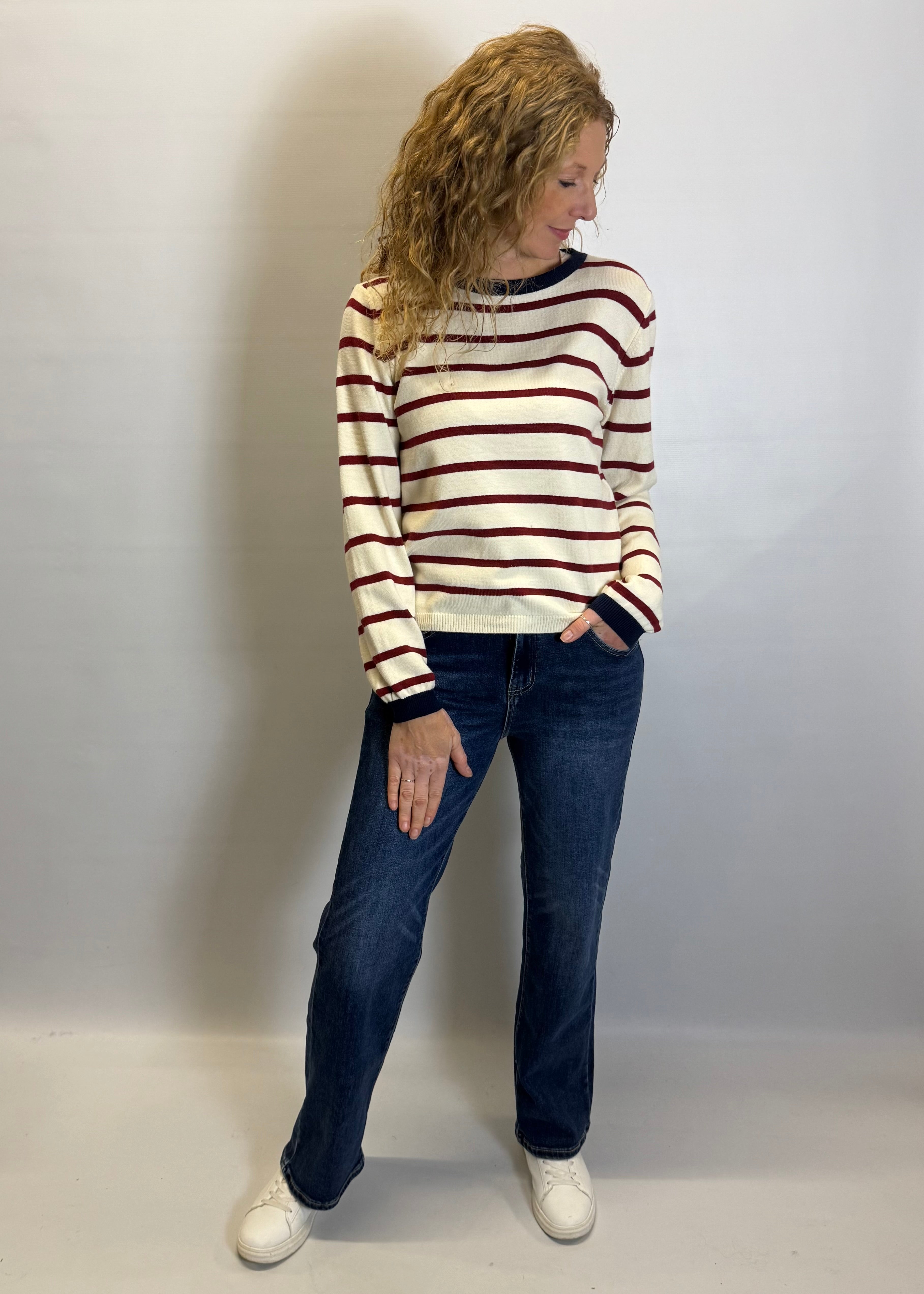 Woman wearing a striped sweater and jeans against a plain background