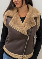 A close-up of a person wearing a brown faux-leather aviator-style vest with a thick beige sherpa collar and lining, over a black long-sleeve top.