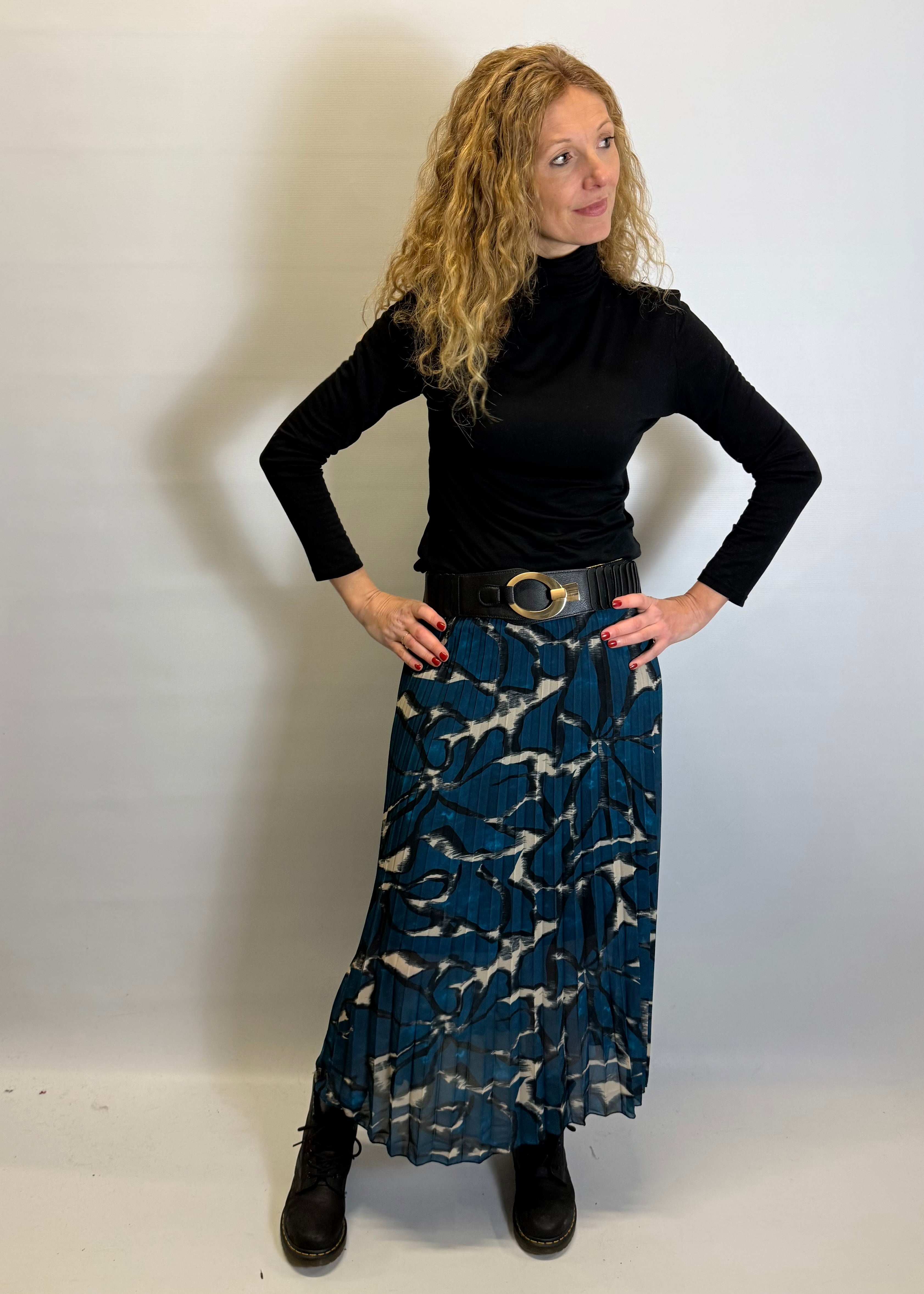 Woman wearing a black turtleneck and blue patterned skirt against a white background