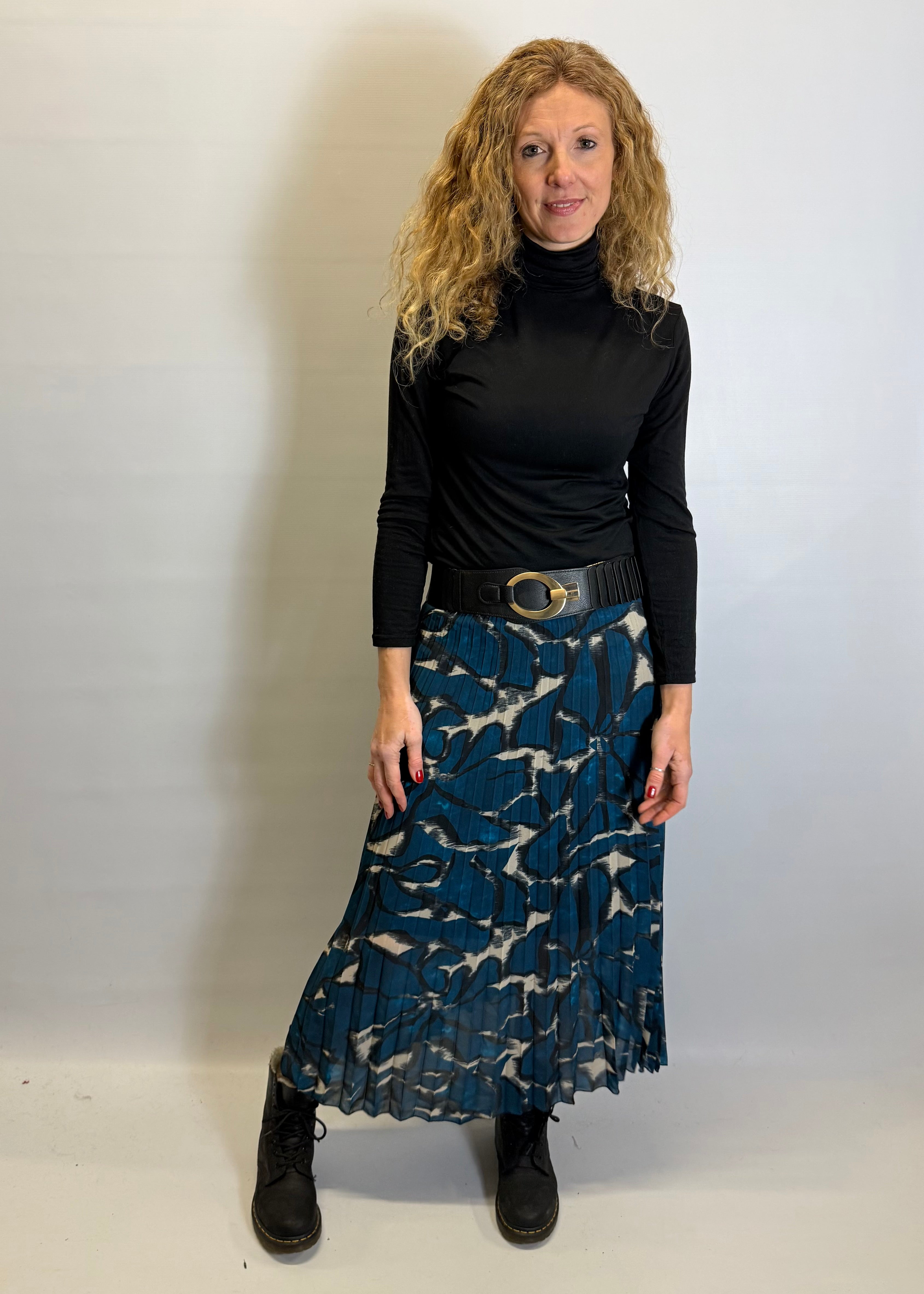 Woman wearing a black turtleneck and blue patterned skirt against a white background