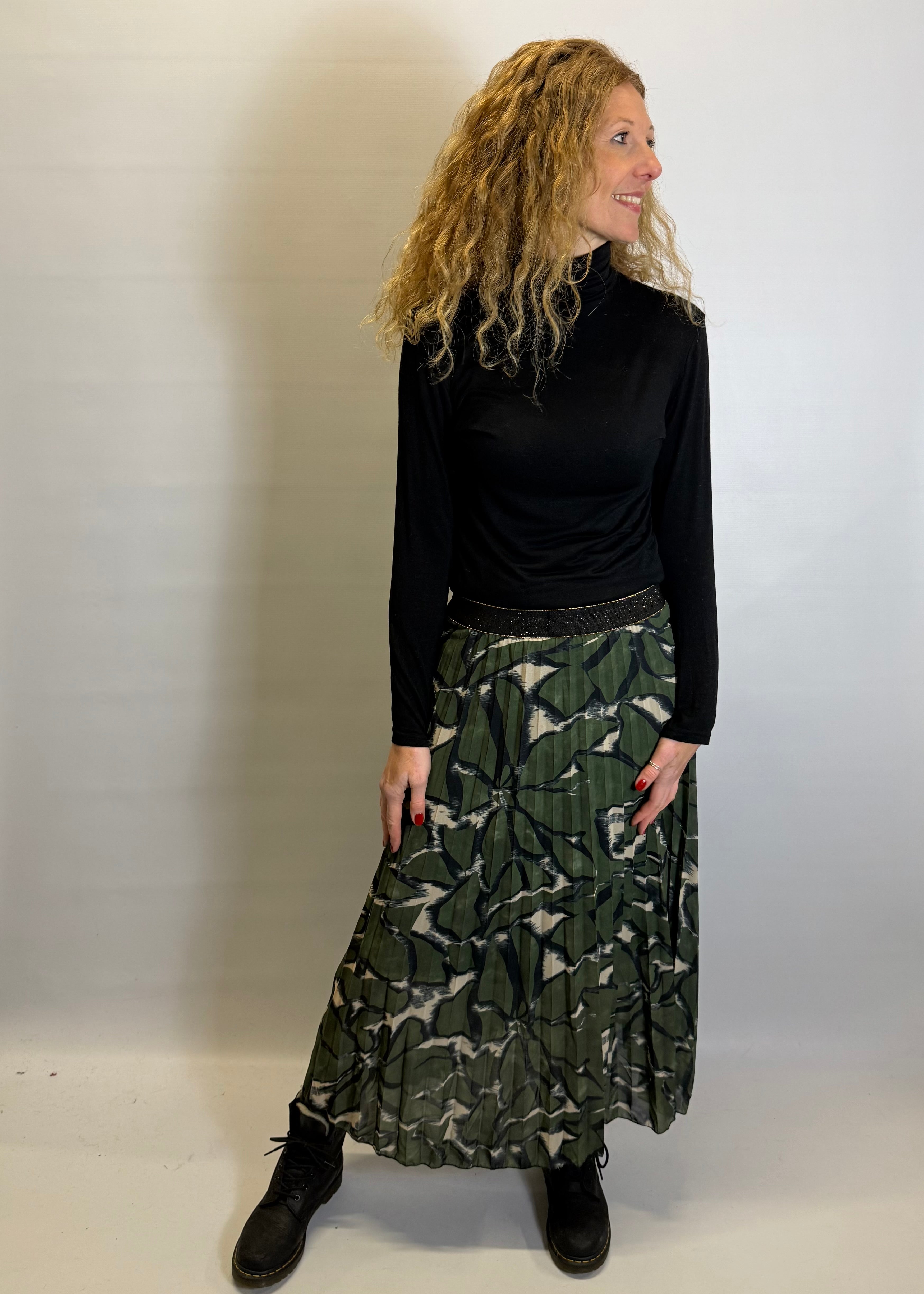 Woman wearing a black long-sleeve top and green patterned skirt against a white background