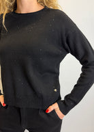 Person wearing a black sweater with sparkle stones on a plain background