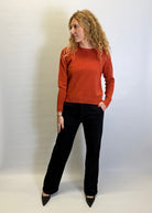 Woman wearing a rust-colored sweater and black pants against a white background
